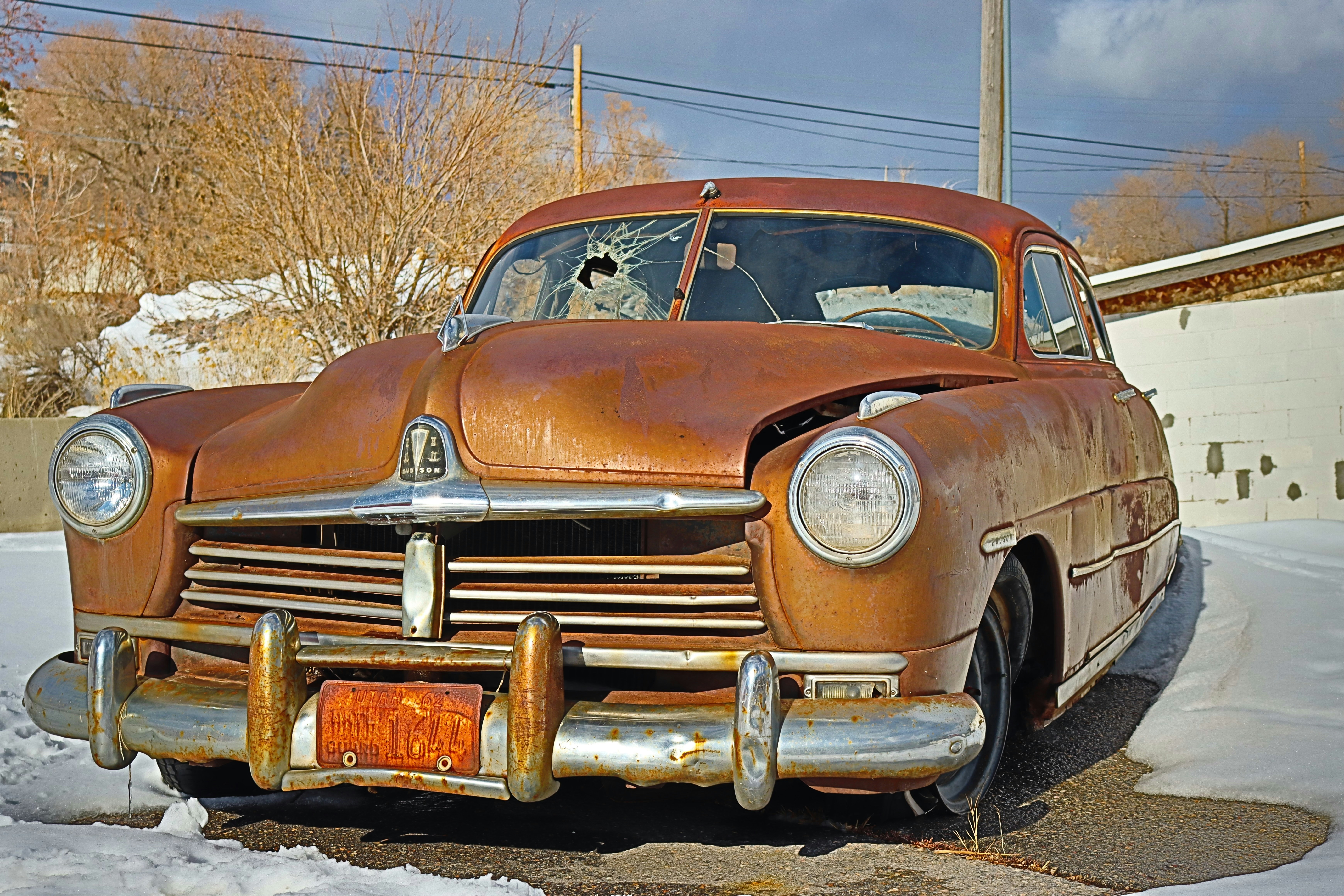 A rusty vintage car sits in the snow.