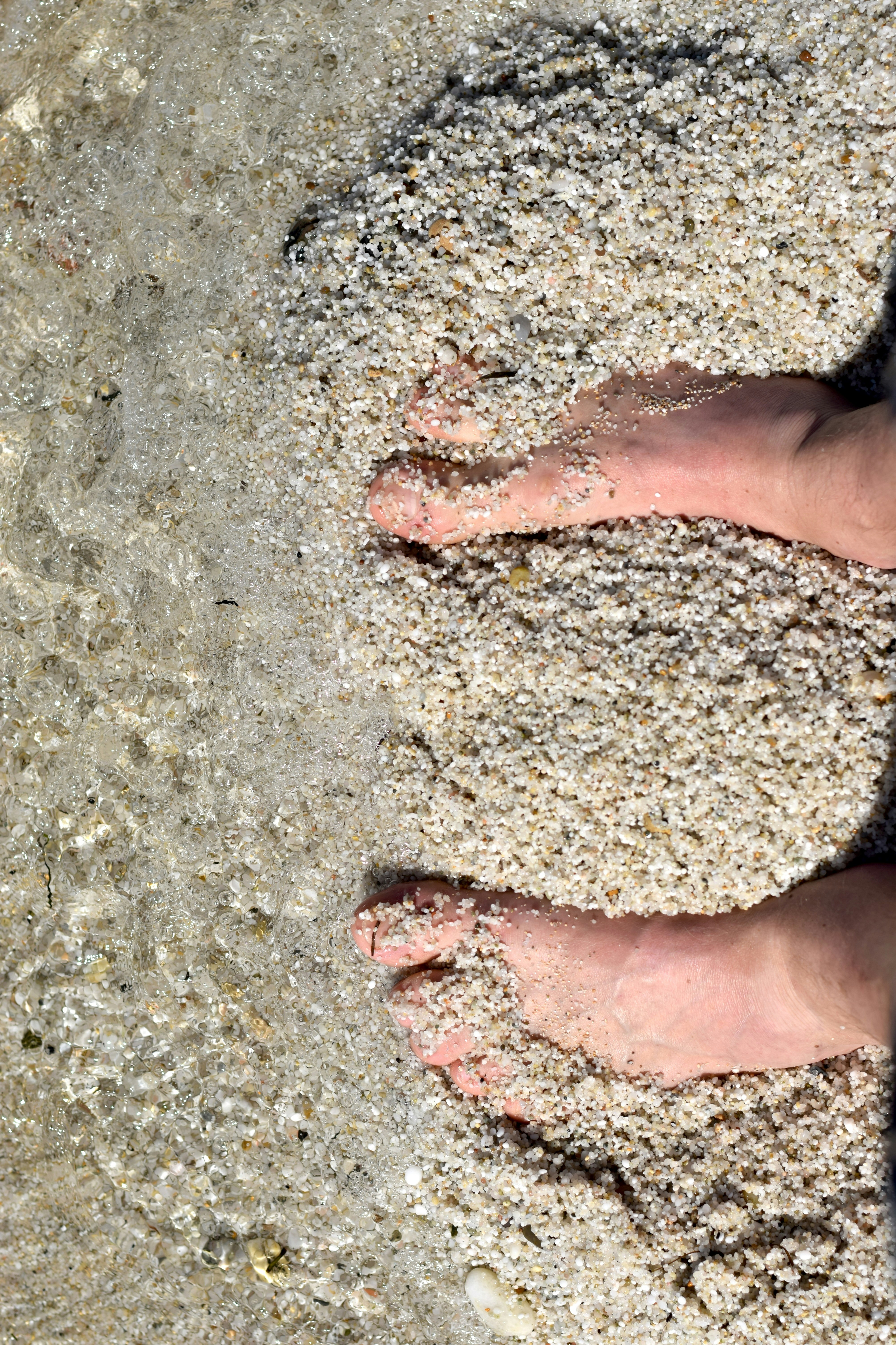 Piedi sepolti nella sabbia al bordo dell'acqua