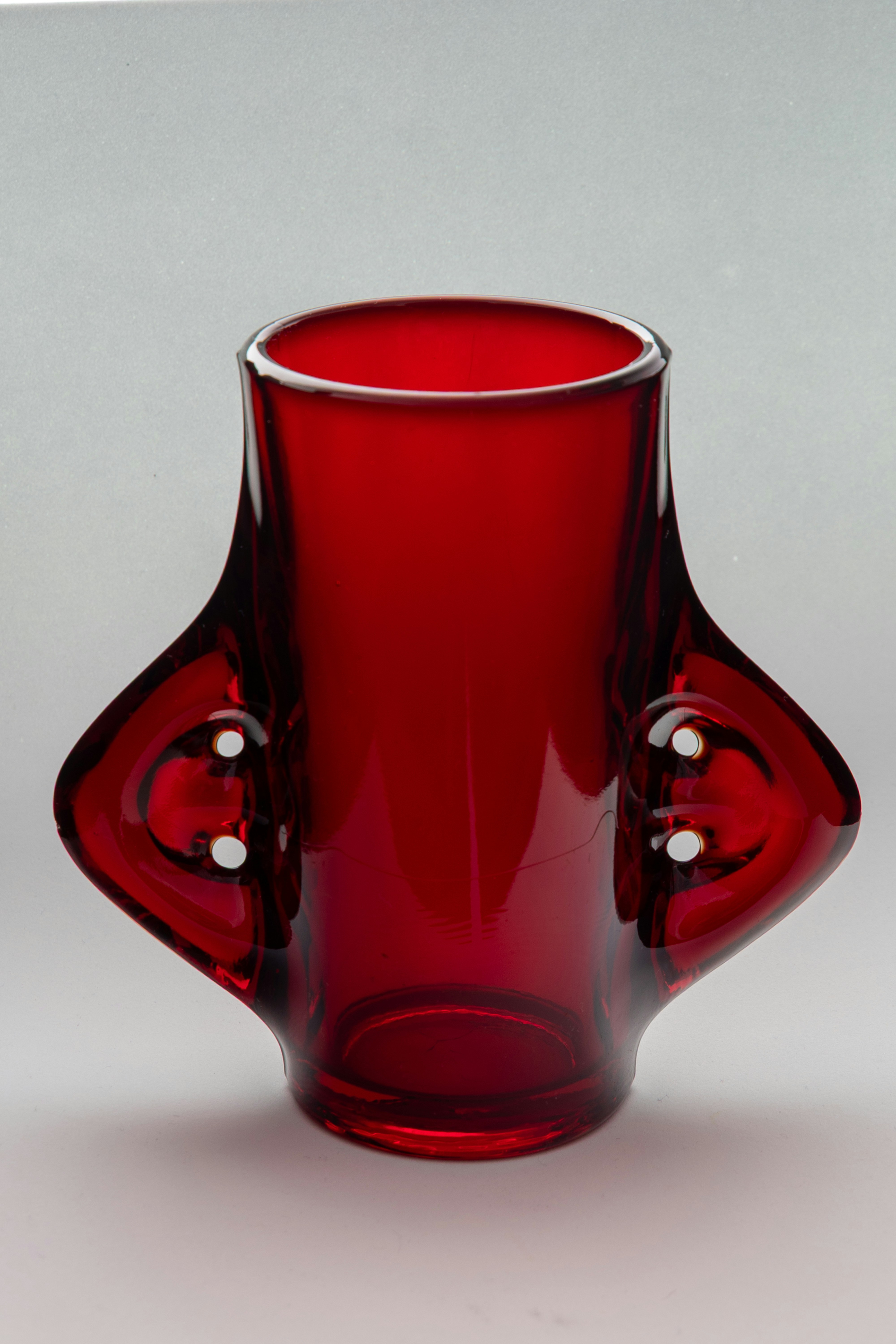 Un petit vase en verre rouge avec deux anses.