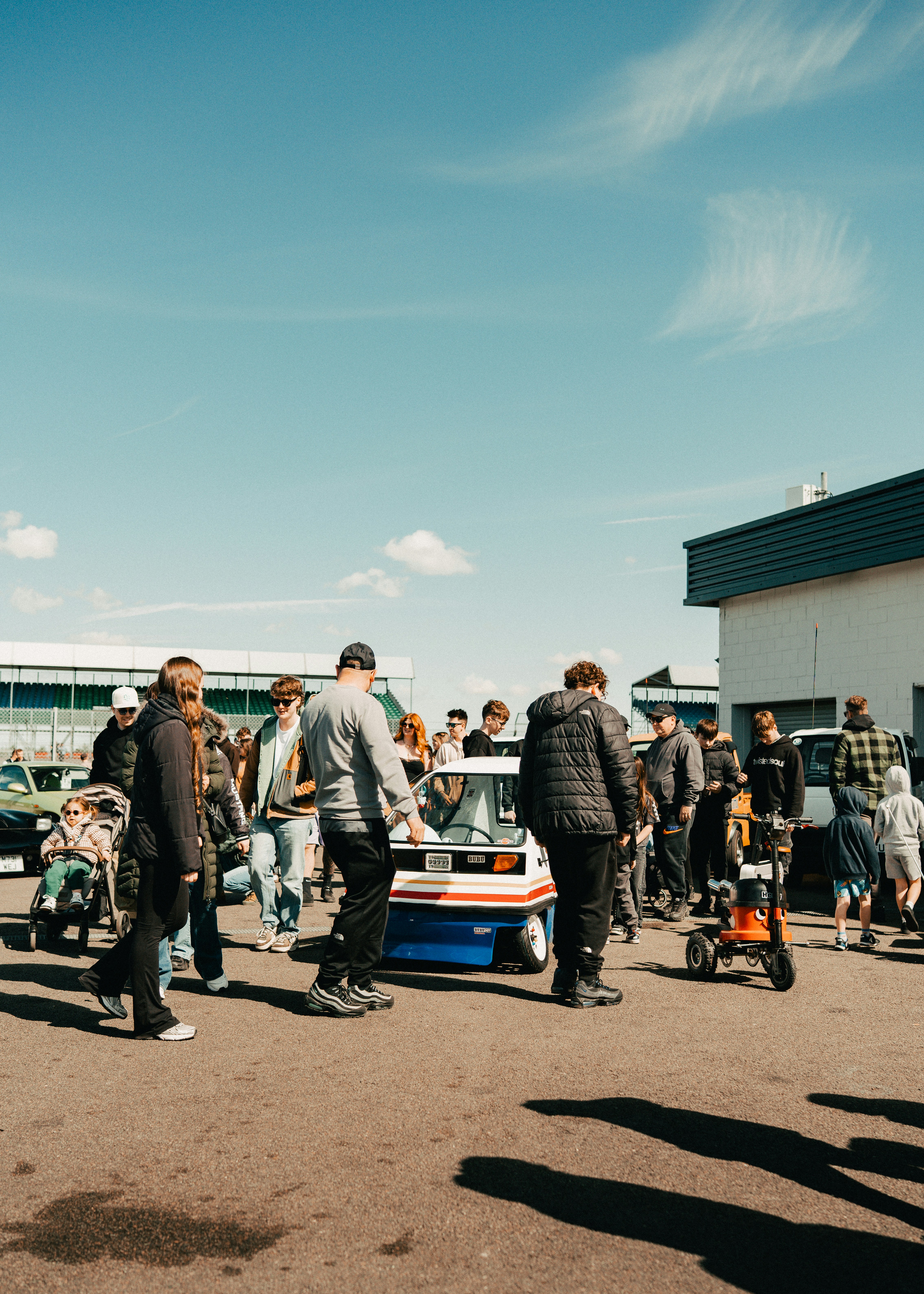 People gathered around a small white and blue vehicle outdoors.