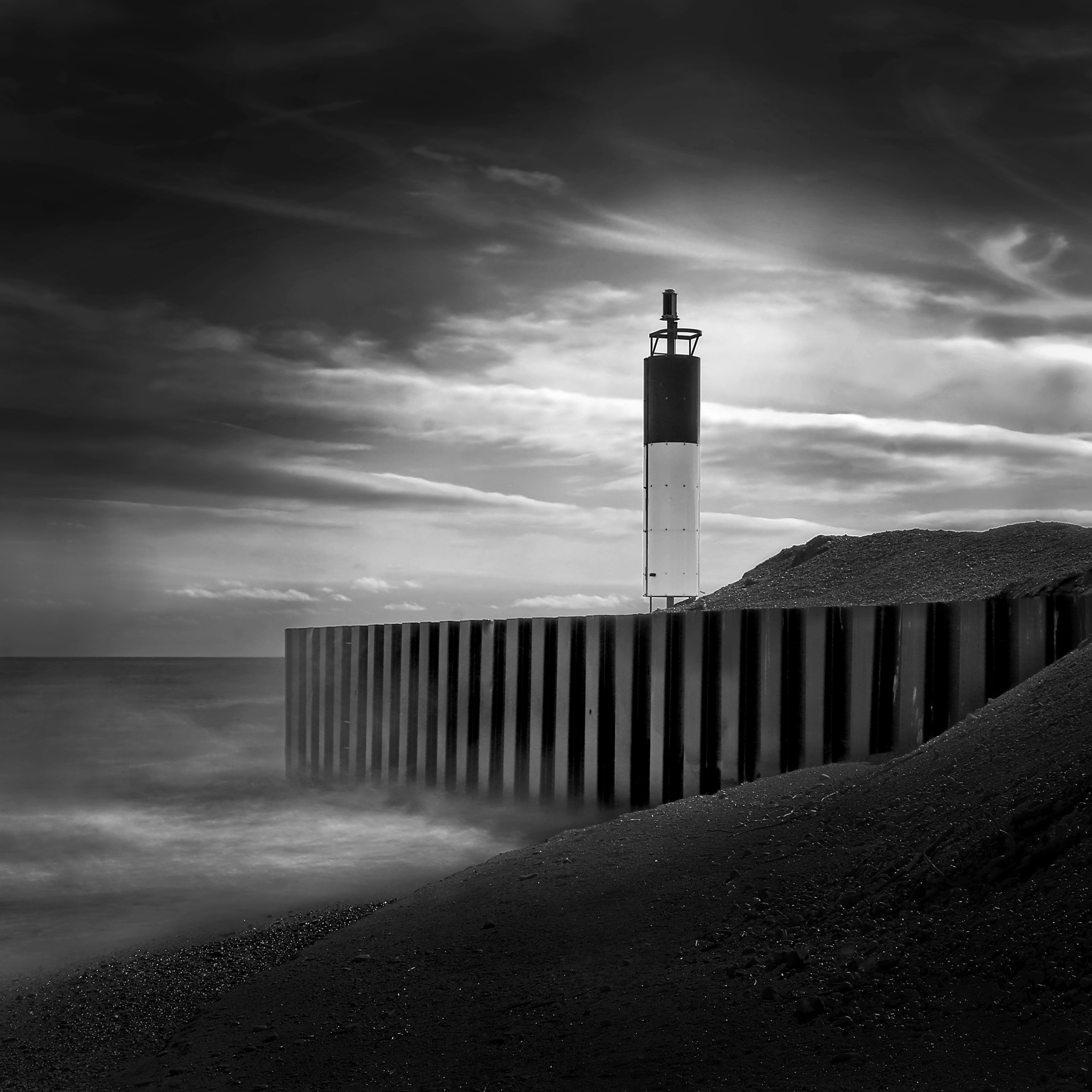 Lighthouse on a stormy coast with wooden barrier.