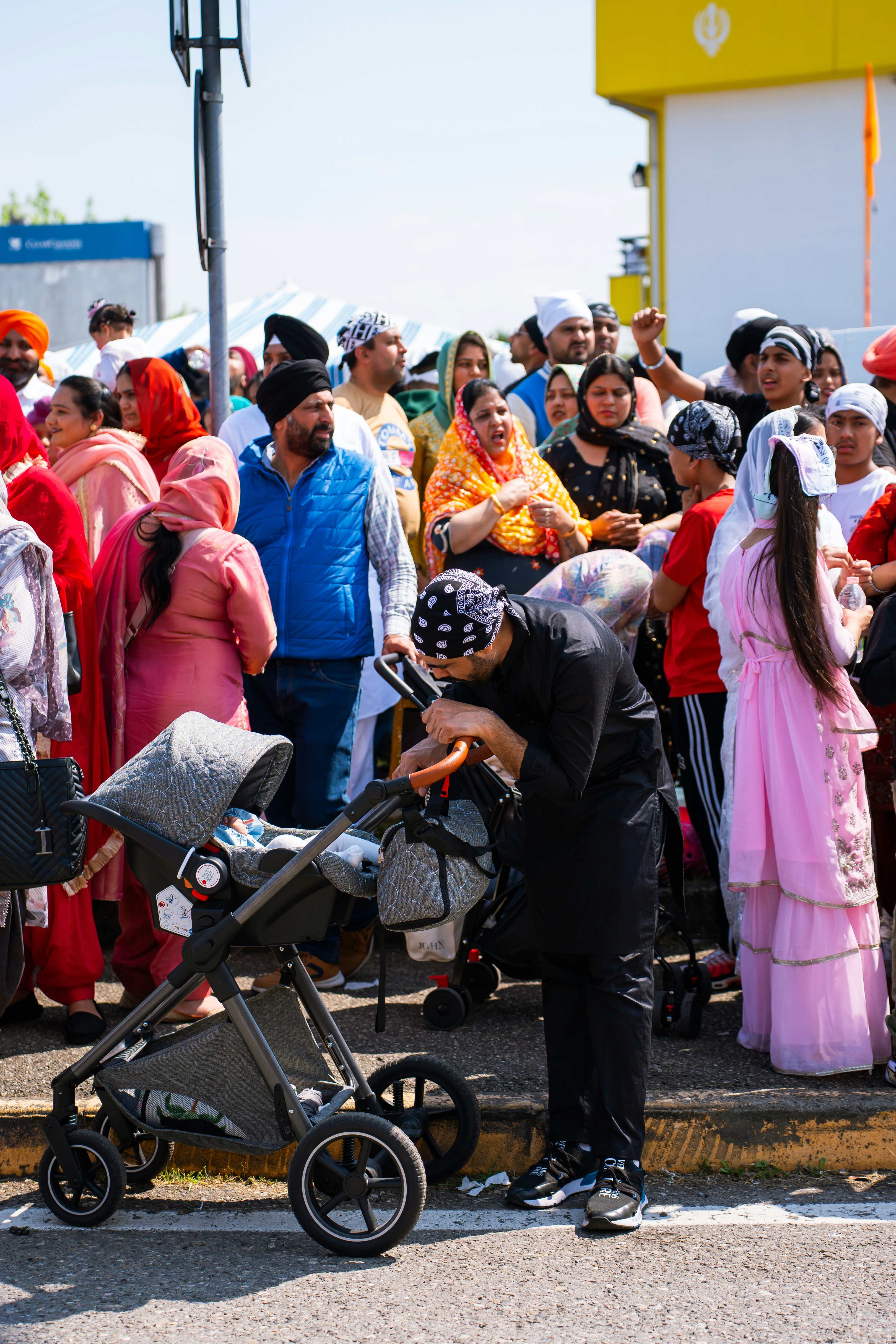 Menschen in traditioneller Kleidung versammeln sich draußen mit einem Kinderwagen.