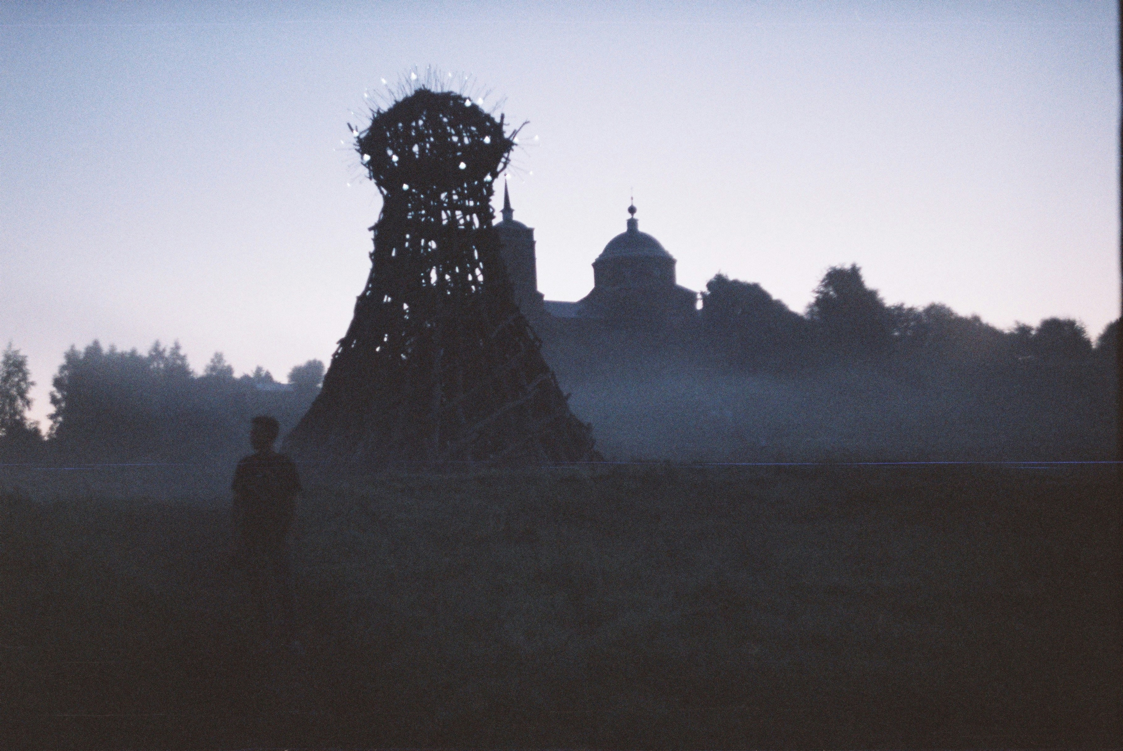 Silhouette d’une personne et d’un grand feu de joie au crépuscule.