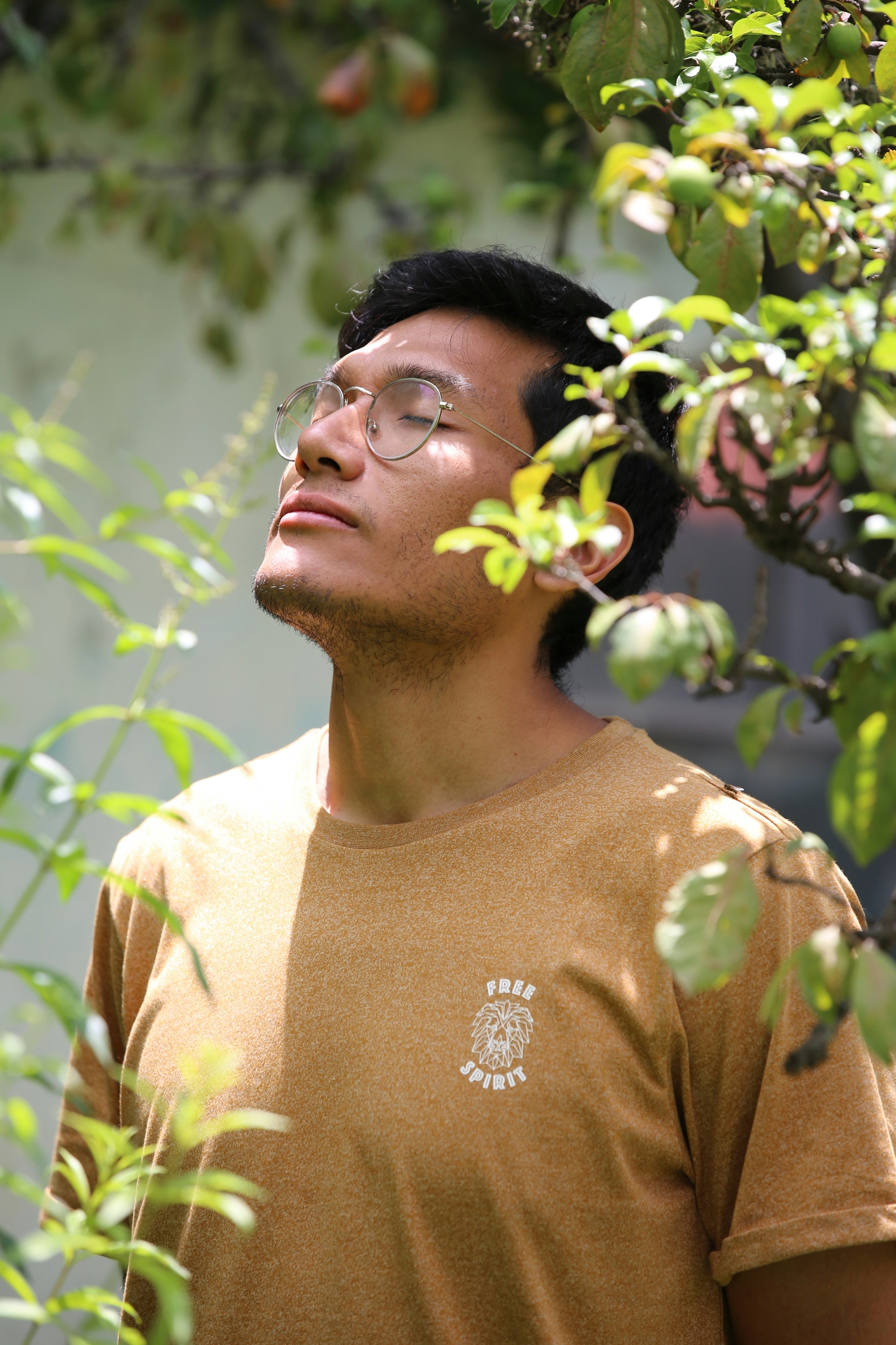 Young man with glasses enjoying sunlight outdoors, eyes closed