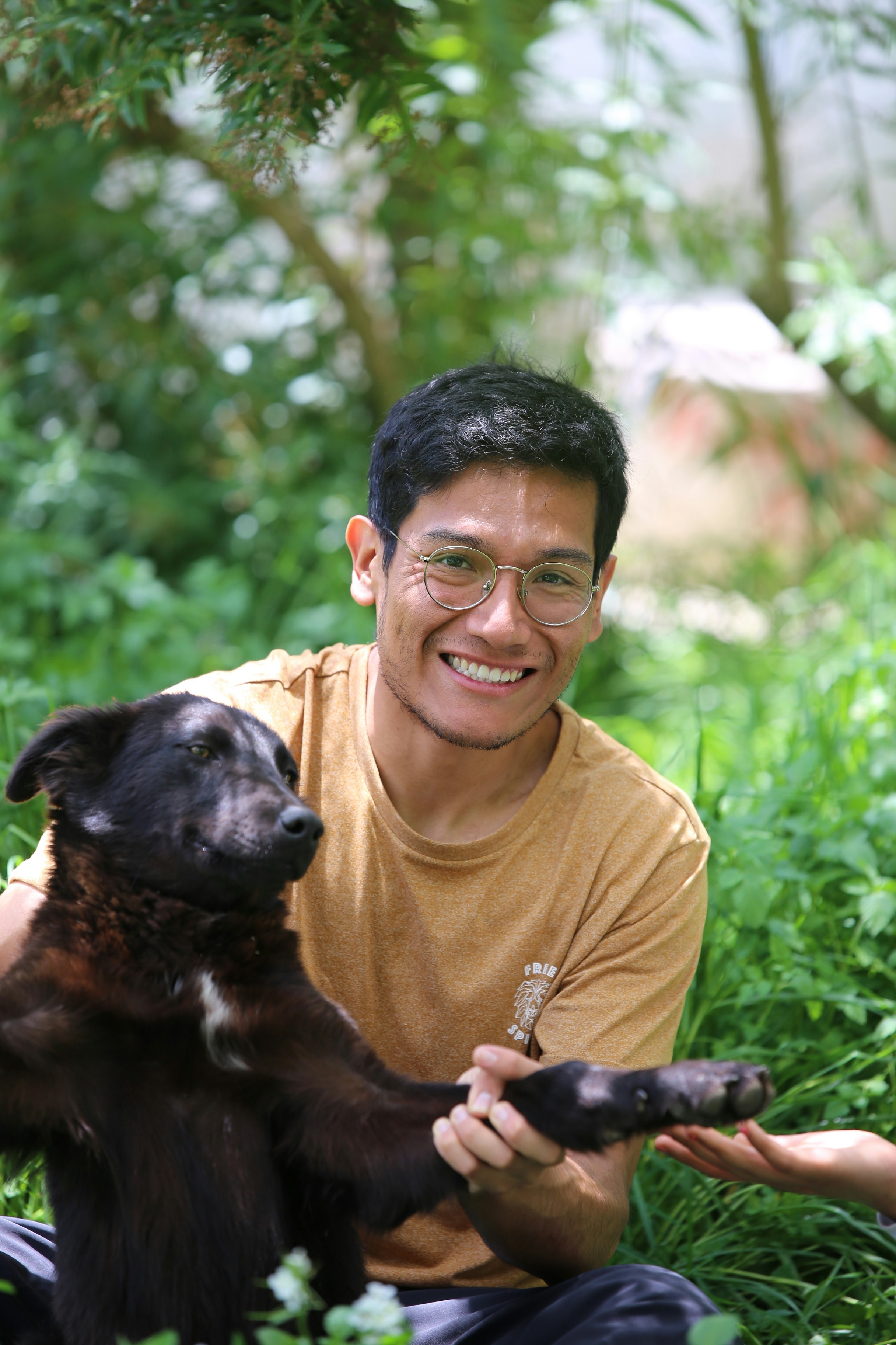 Man smiling, holding a black dog's paw outdoors