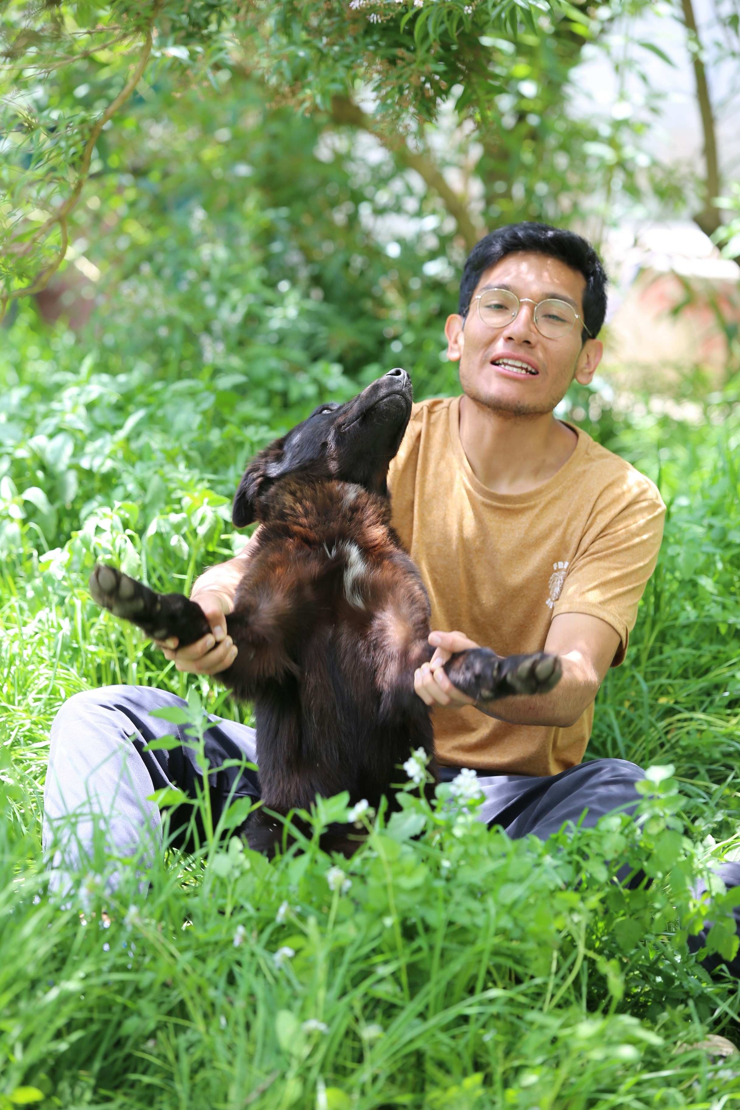 Smiling man holding a black dog in lush green grass