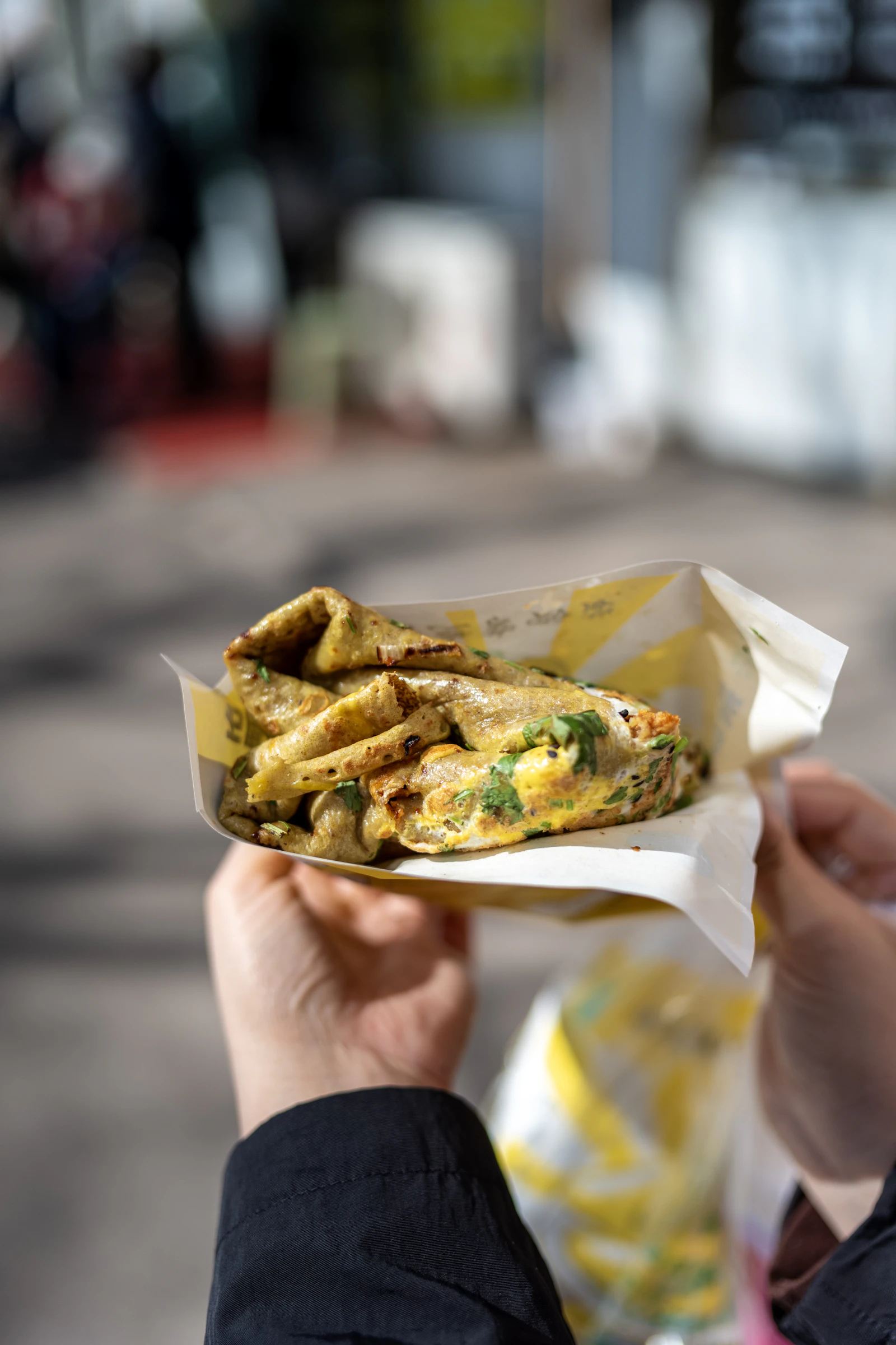 Hand holding a folded wrap with herbs and fresh toppings