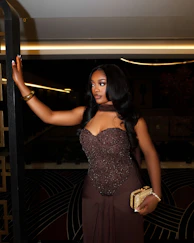A woman in a brown dress holding a clutch bag.