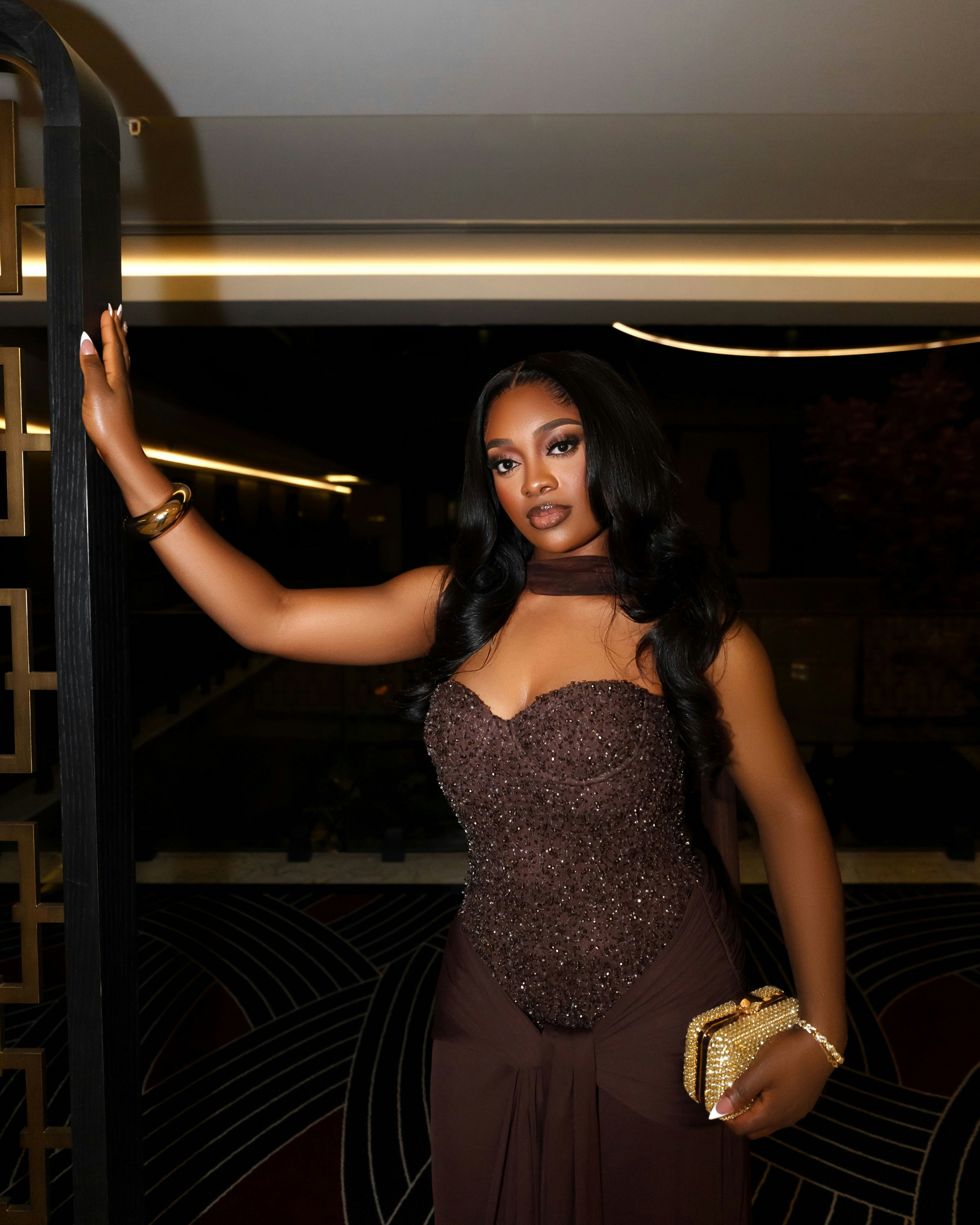 A woman in a sparkling brown dress holds a clutch.