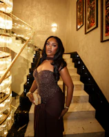 A woman in a brown dress poses on a staircase.