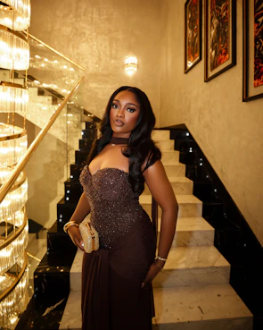 A woman in a brown dress poses on a staircase.