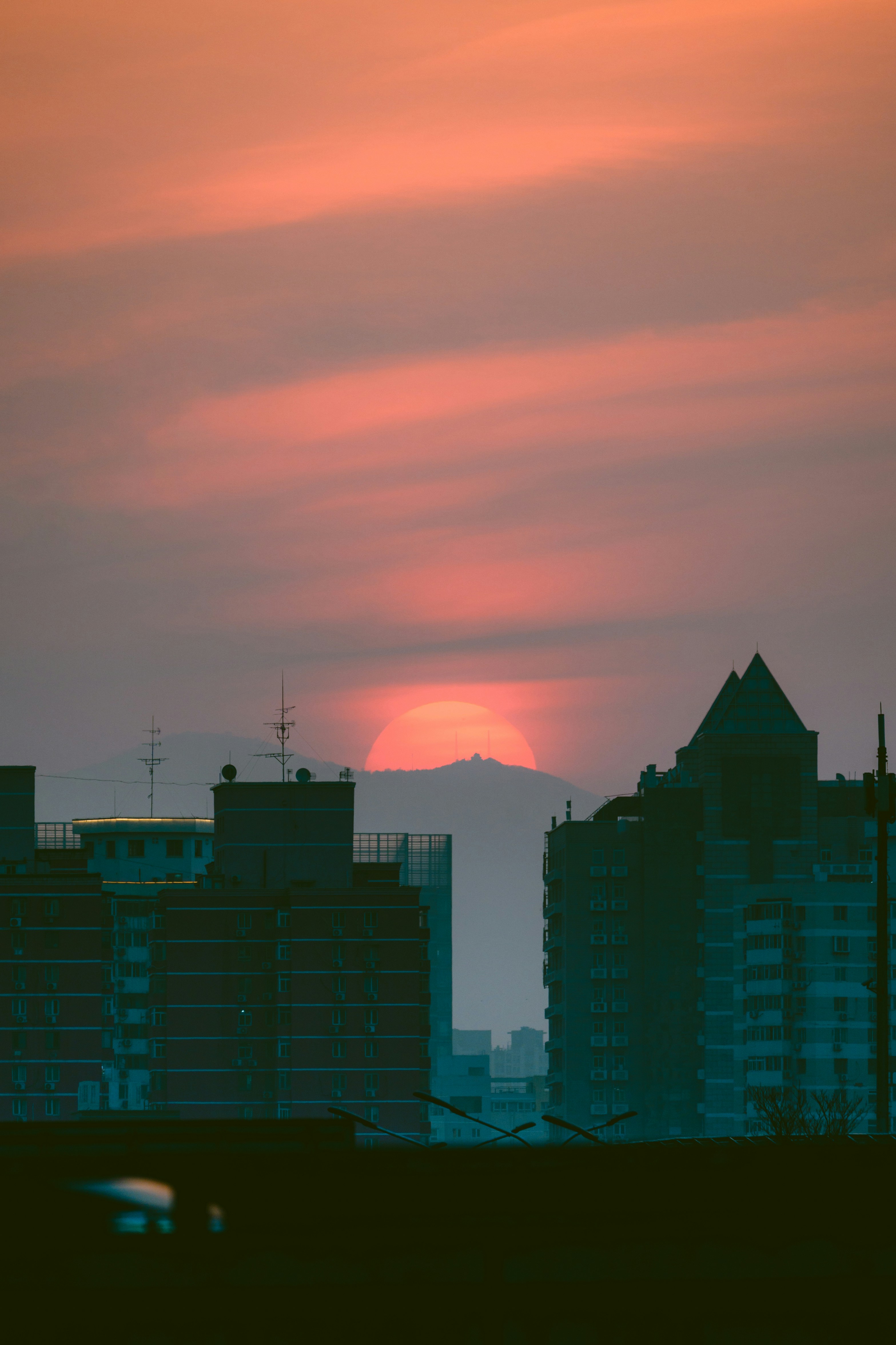 Atardecer tras montañas lejanas sobre edificios de la ciudad.