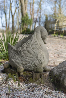 Stone swan sculpture sits on a tree stump.