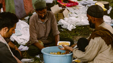 Three men sharing food from a communal bowl.