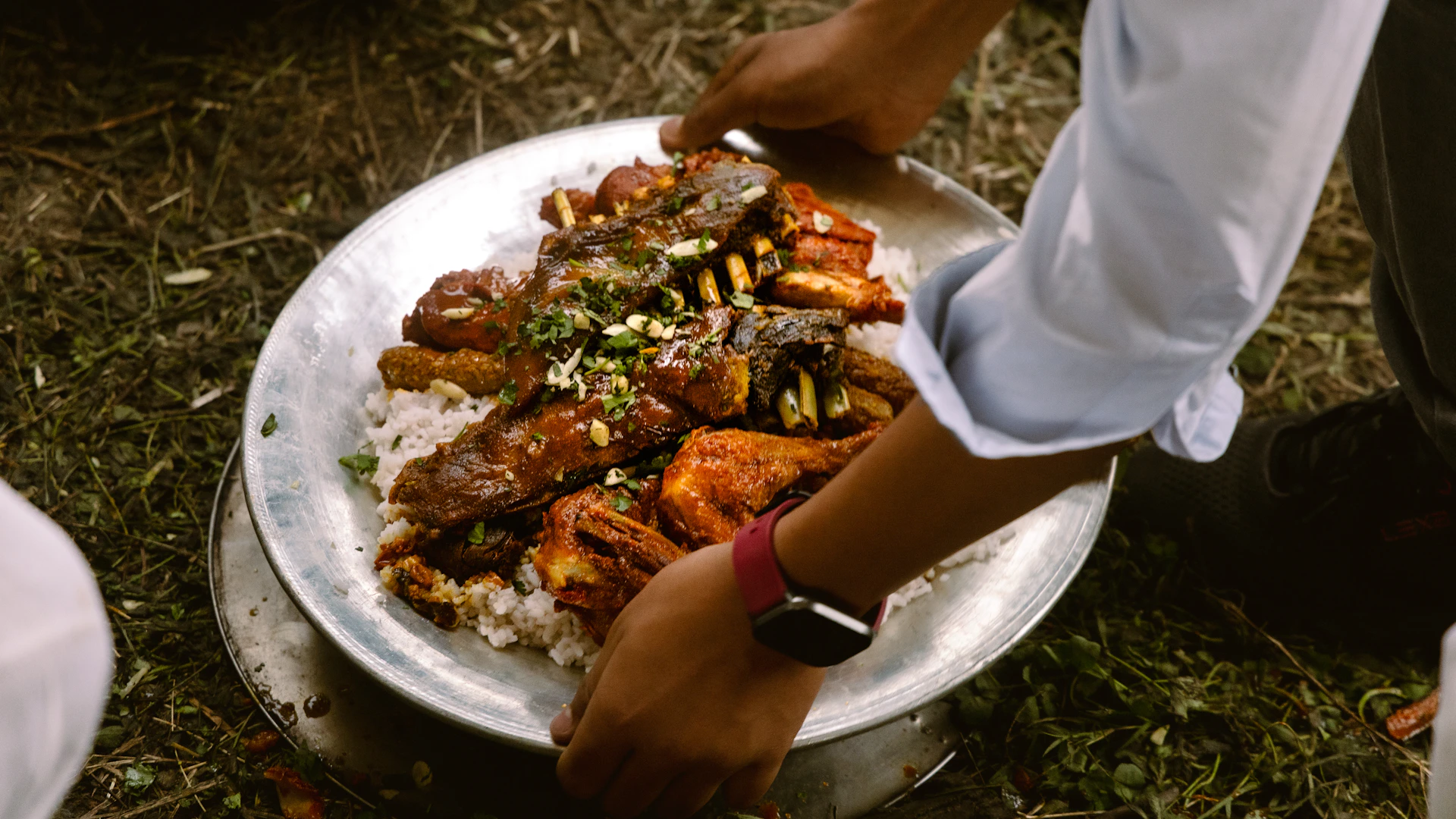 Hands serving a large platter of rice and meat.