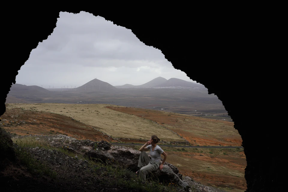 Person sitting on rock inside underground cave with back to camera looking out at landscape