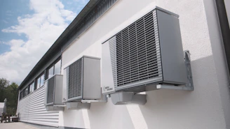 Three gray air conditioning units mounted on a white wall.