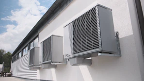 Three gray air conditioning units mounted on a white wall