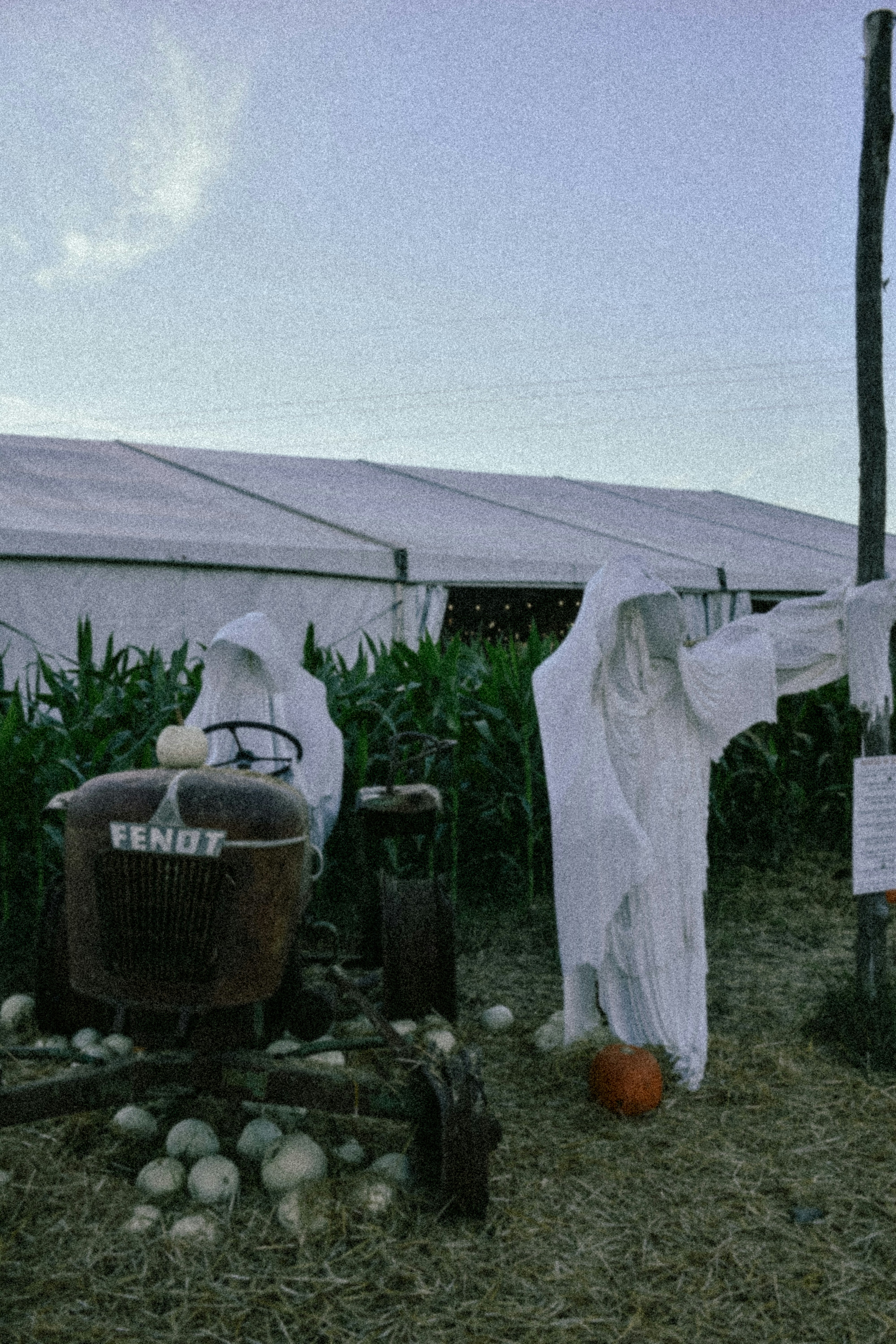 Dua sosok hantu berdiri di dekat traktor vintage dan labu.