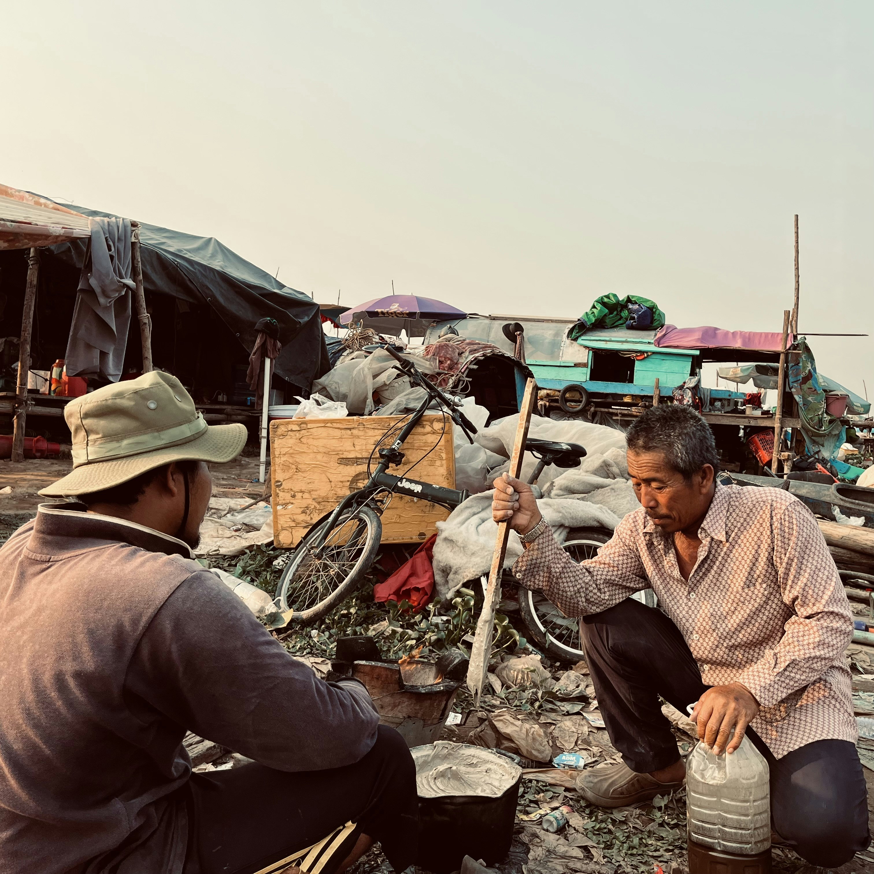 Dois homens cozinhando ao ar livre em um assentamento rústico.