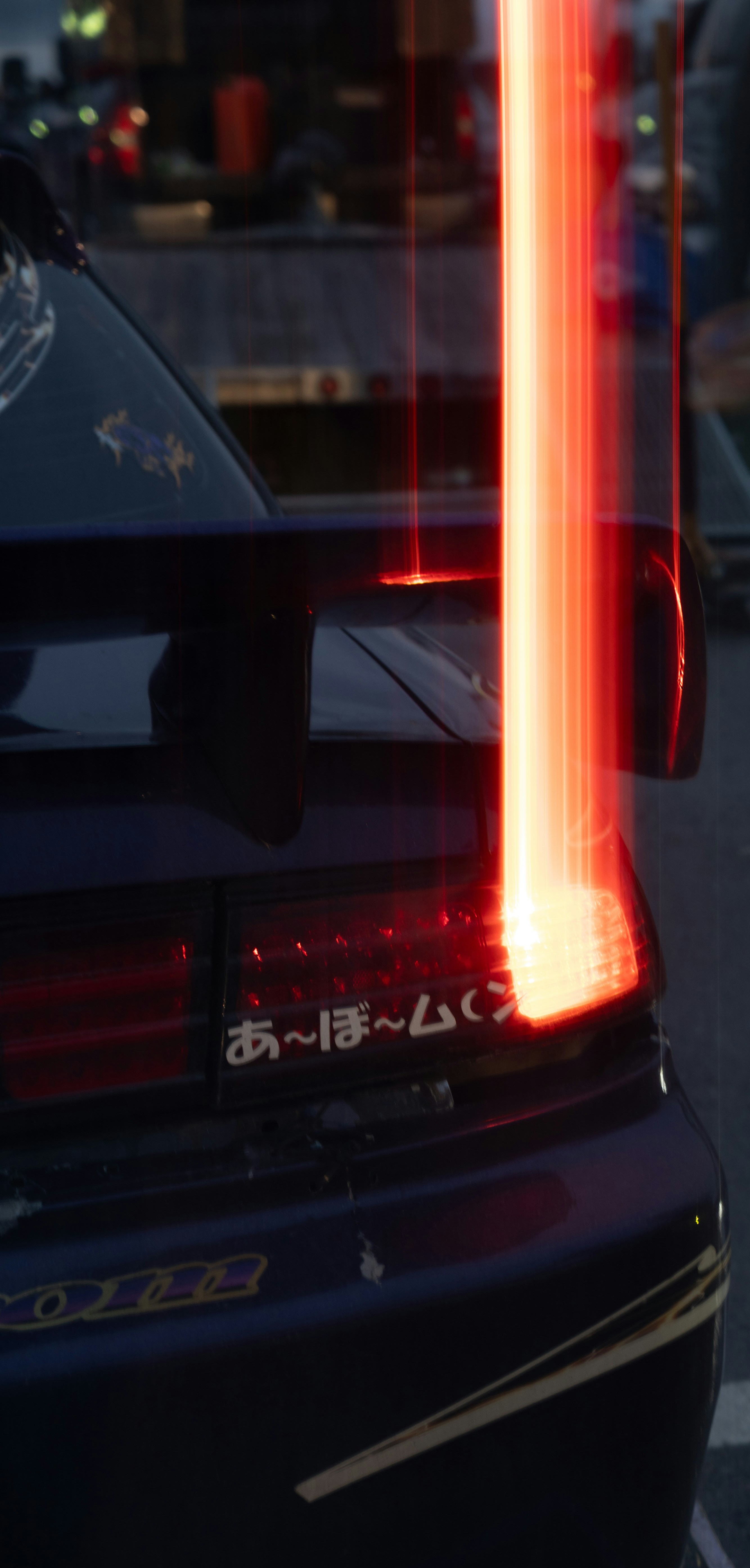 Red light trails streak past a dark blue car's taillight.