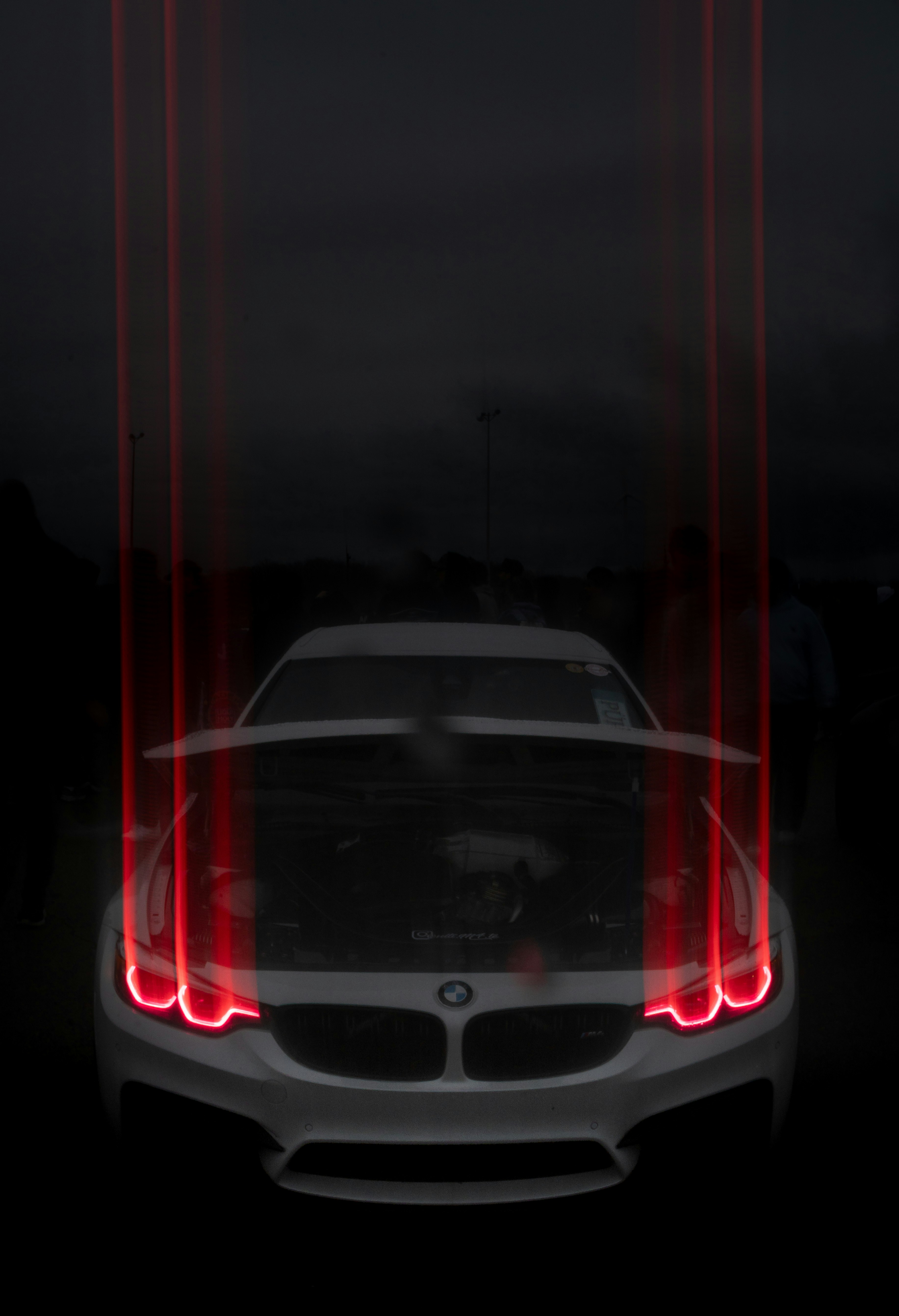 White BMW car with glowing red headlights and hood open.