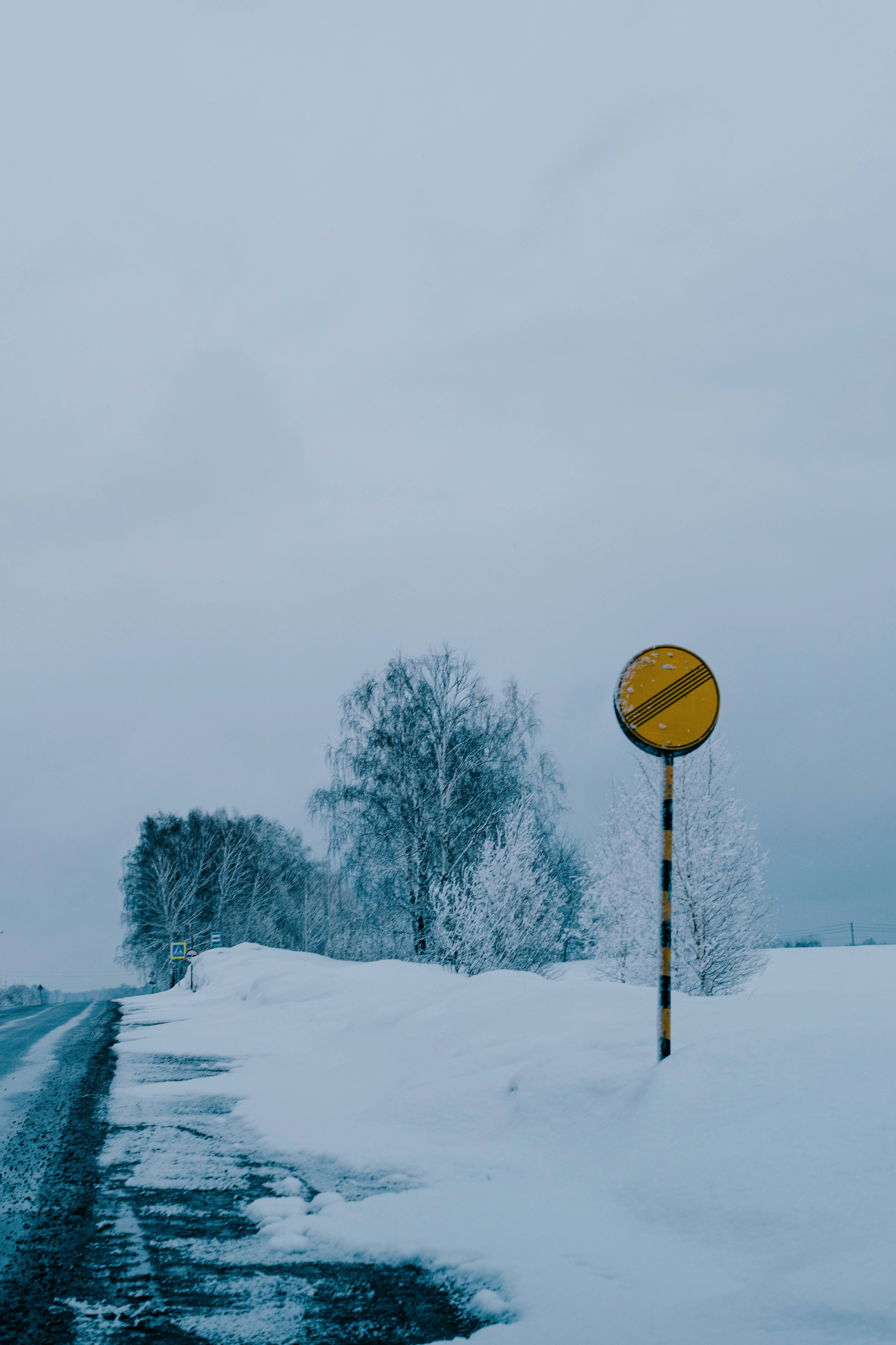 A snowy road with a yellow traffic sign.