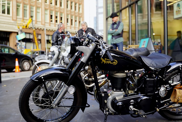 A vintage Norton motorcycle parked on a city street, the marque that will emerge from the dip tank