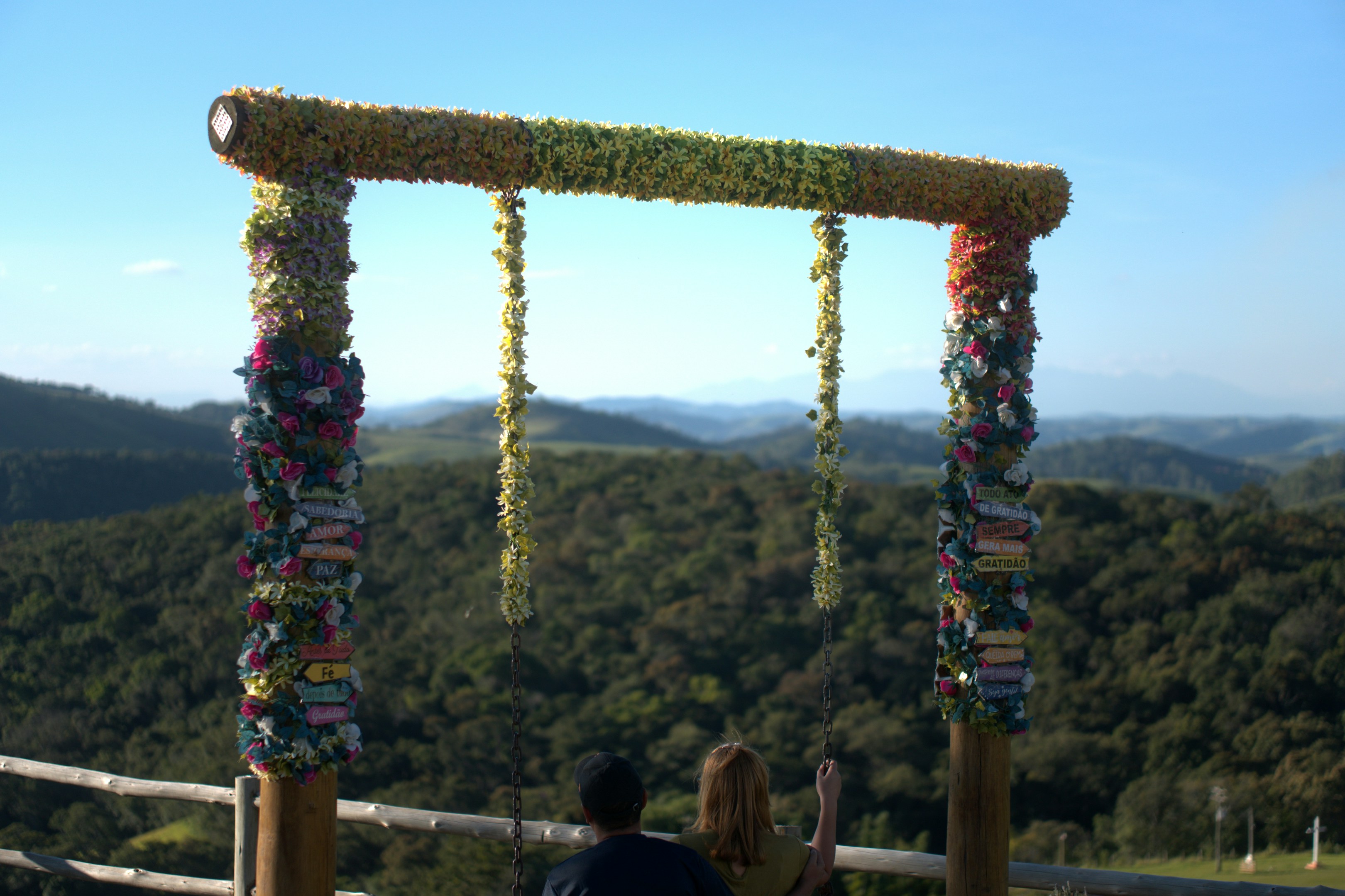 Couple on a swing overlooking a lush green landscape.