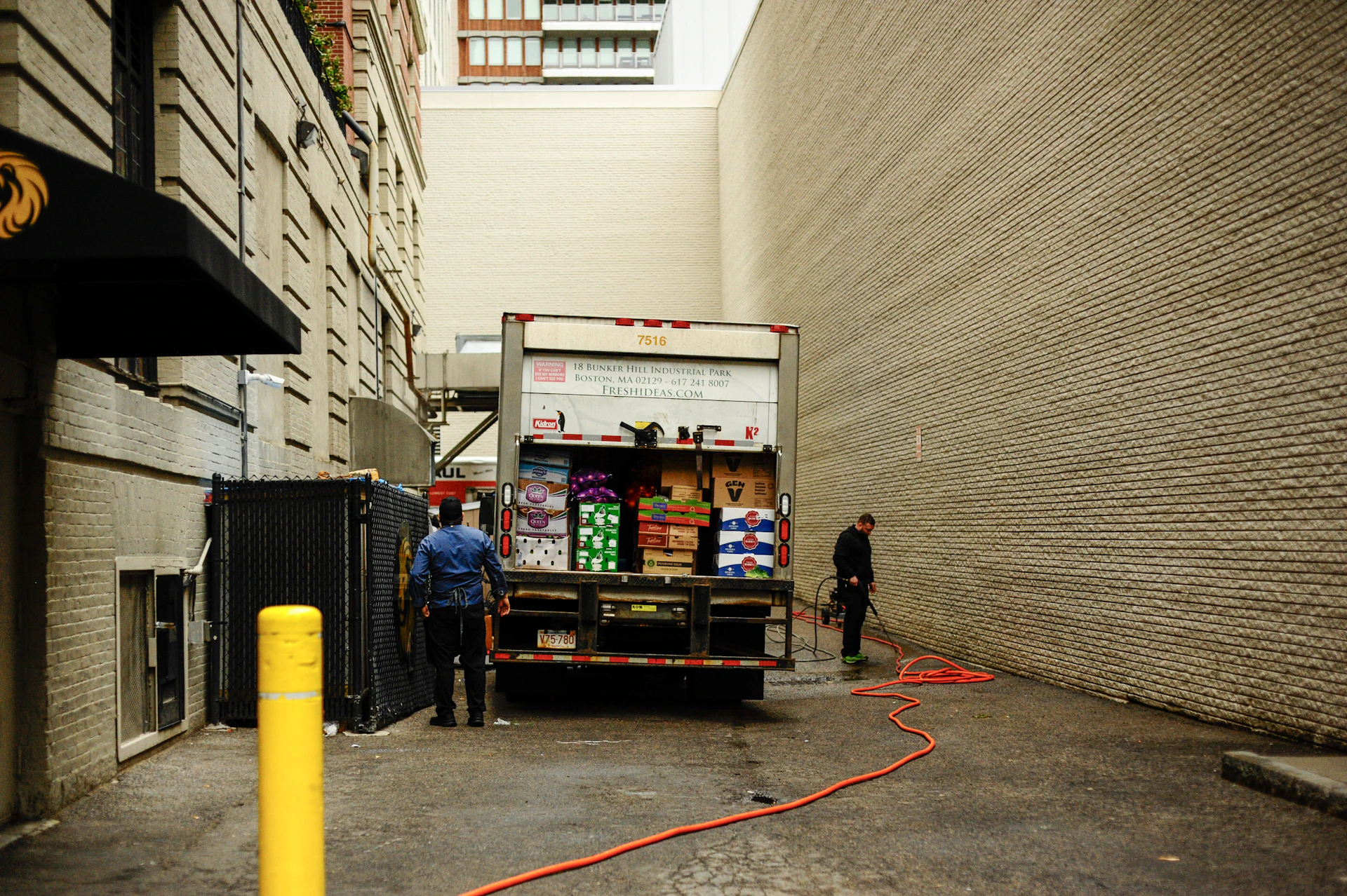 Two men unloading a delivery truck in an alley.