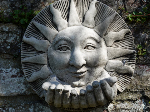 Stone sun face sculpture with outstretched hands