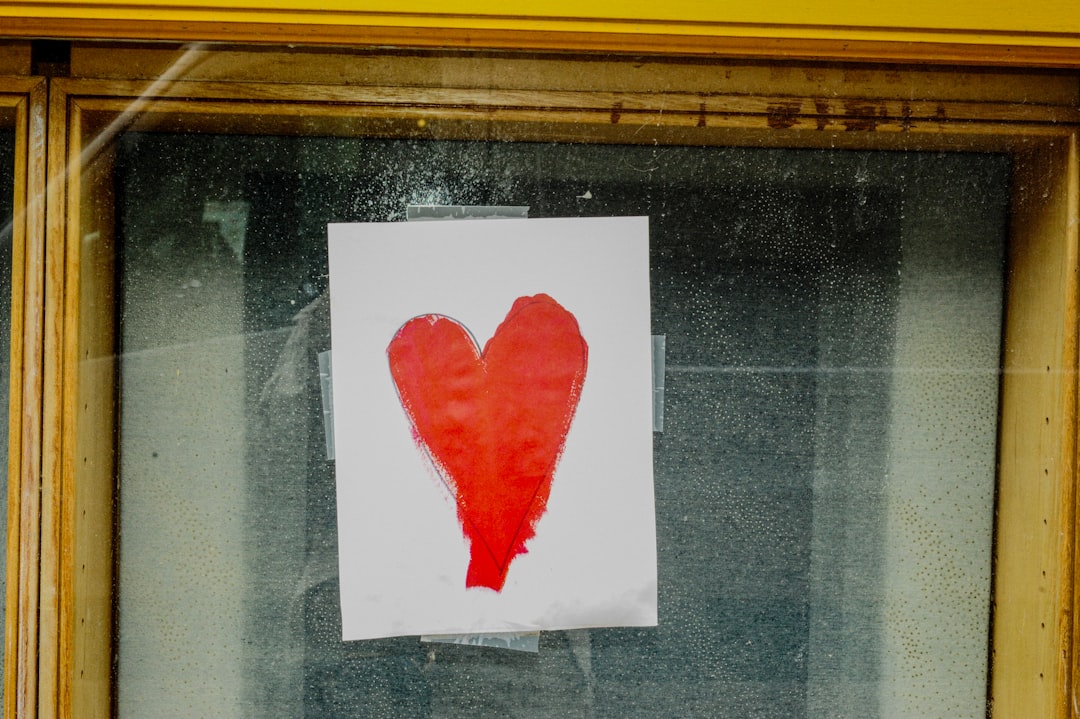 A red heart drawn on white paper taped to glass