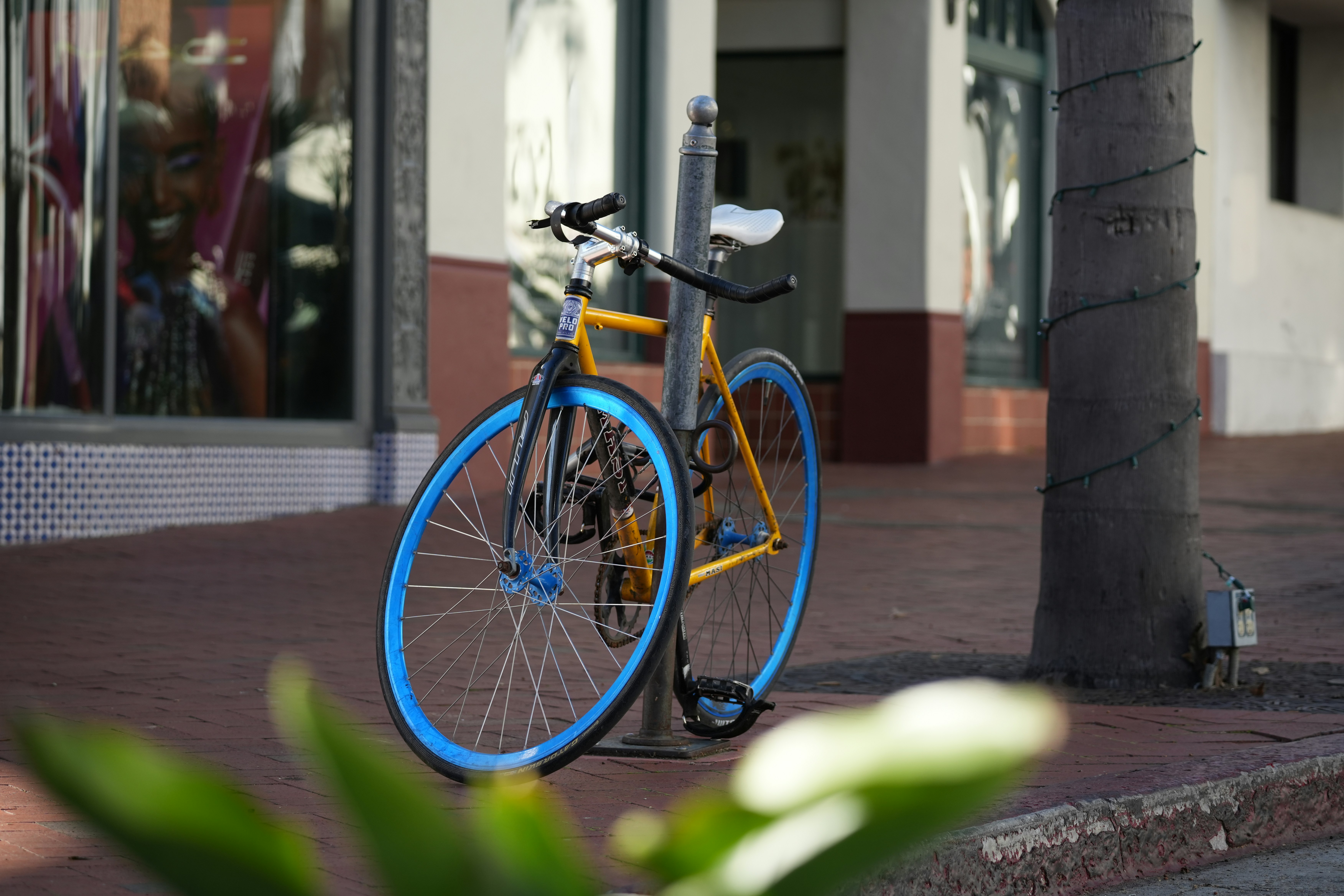 Yellow bicycle with blue rims parked on sidewalk