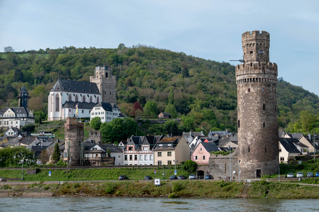 Oberwesel am Rhein mit dem runden Ochsenturm, Kirche und grünen Hängen unter hellem Himmel
