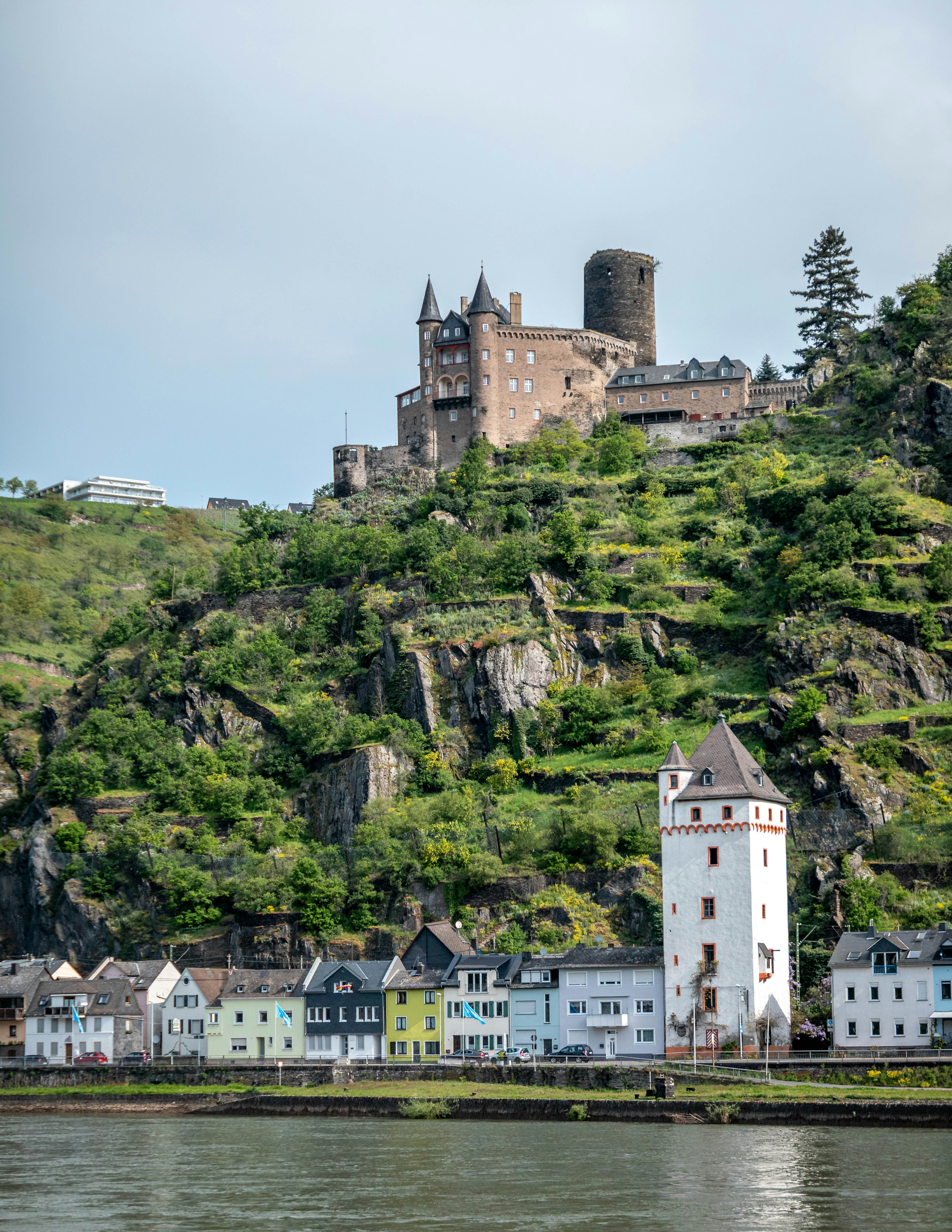 Castle ruins on a green hillside above a river town.