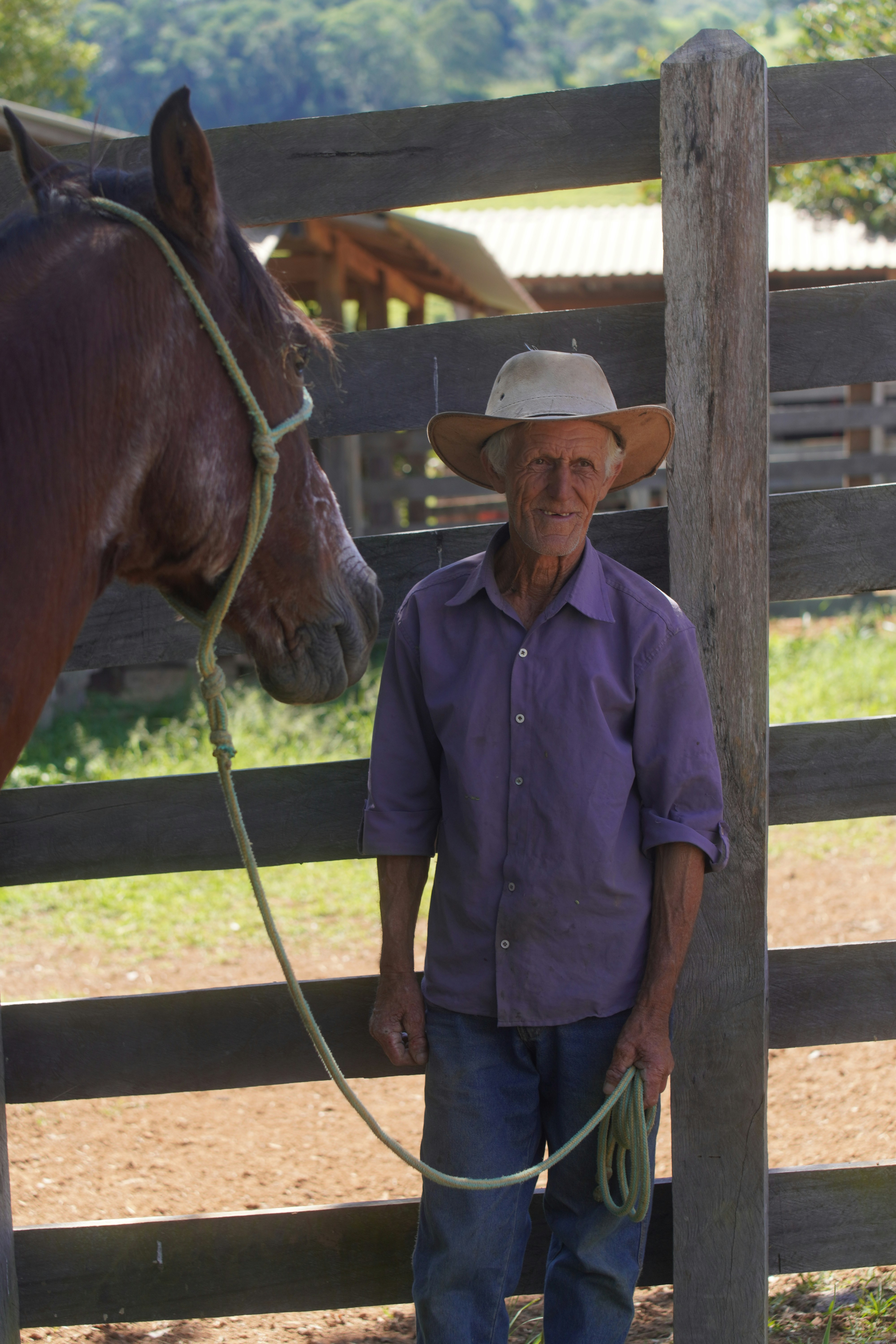 An older man in a hat stands with a horse.