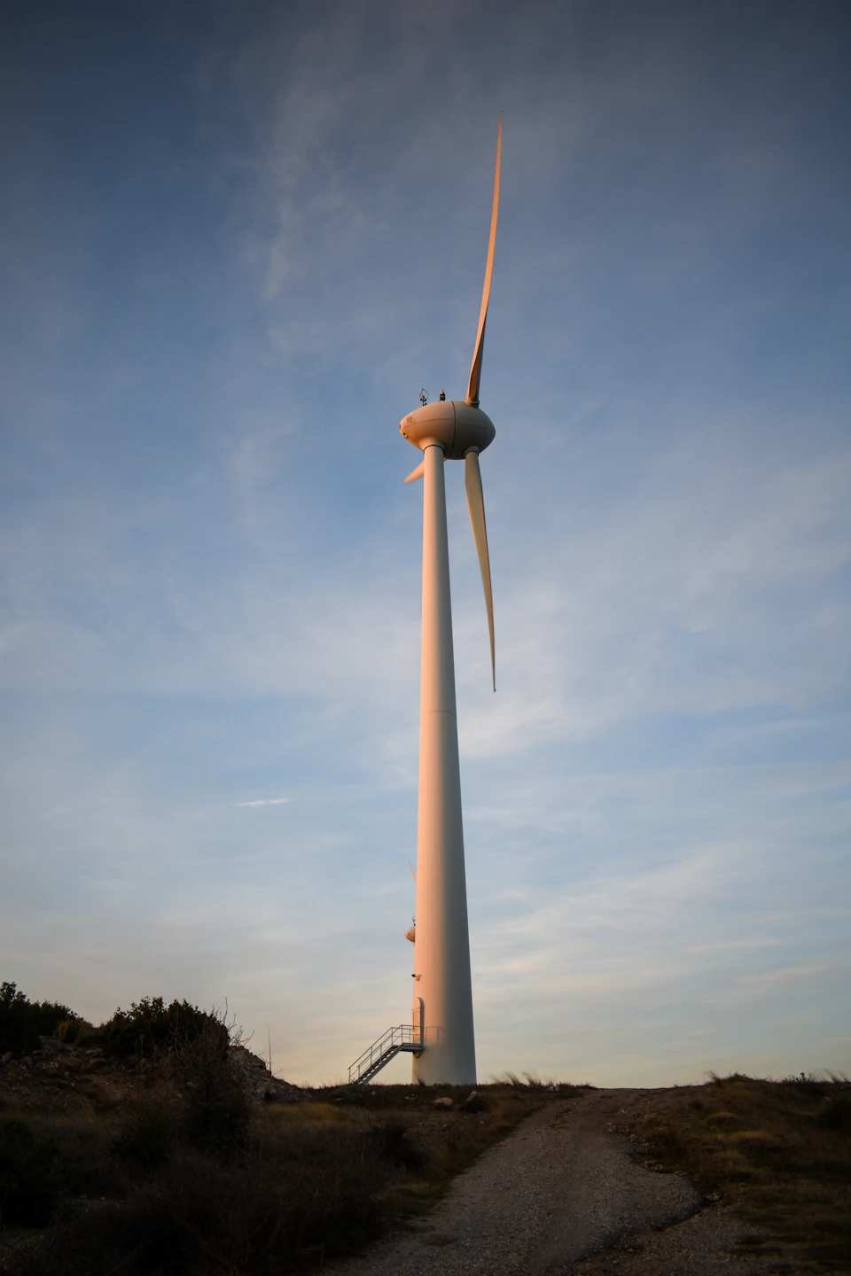 Large white wind turbine stands tall on a hill with its blades facing right