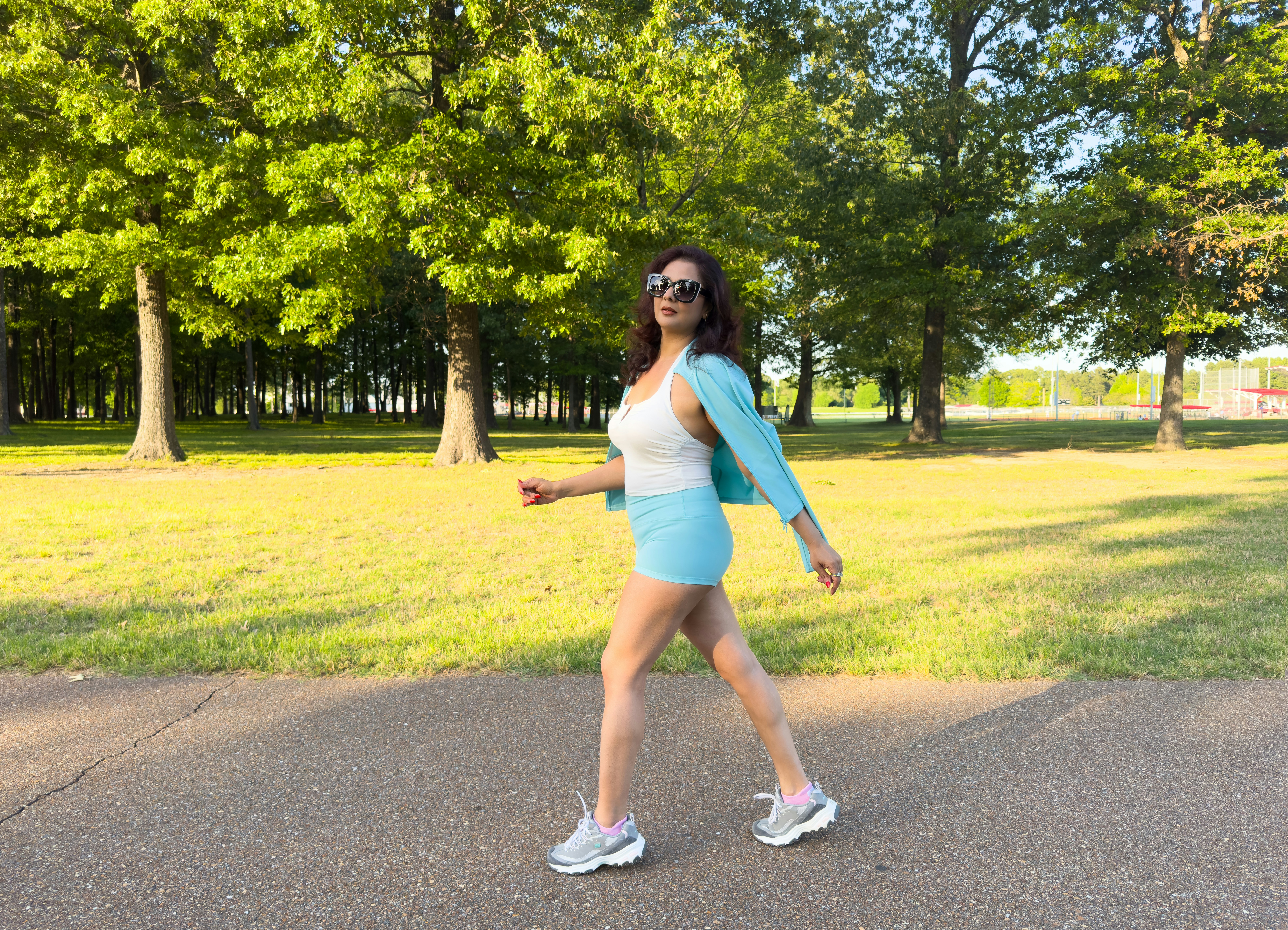 A woman walks on a paved path in a park.