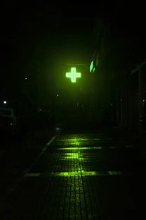 Green illuminated cross sign at night on wet street