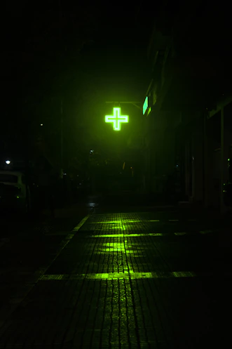 Green illuminated cross sign at night on wet street