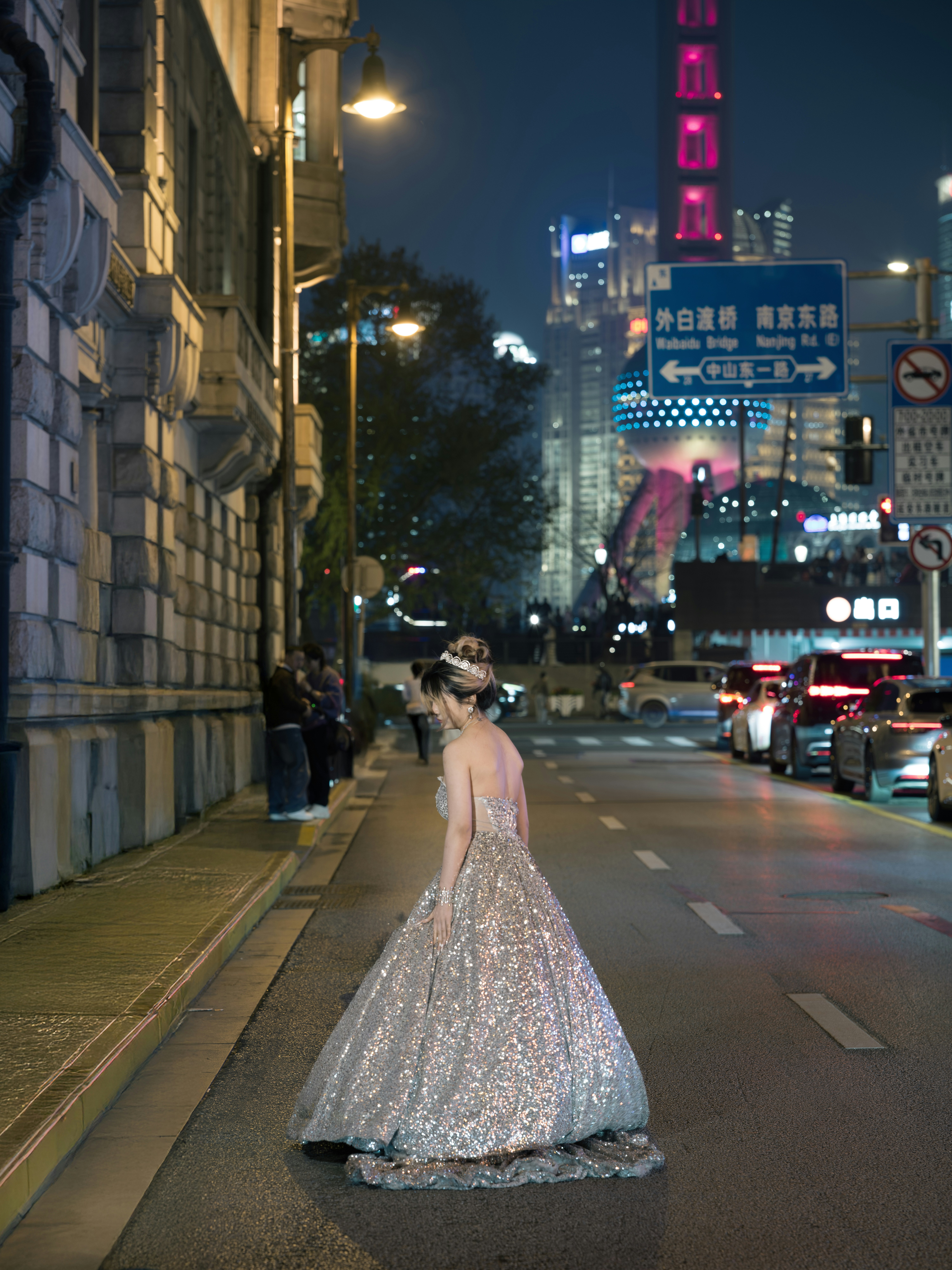 Woman in sparkling gown on city street at night