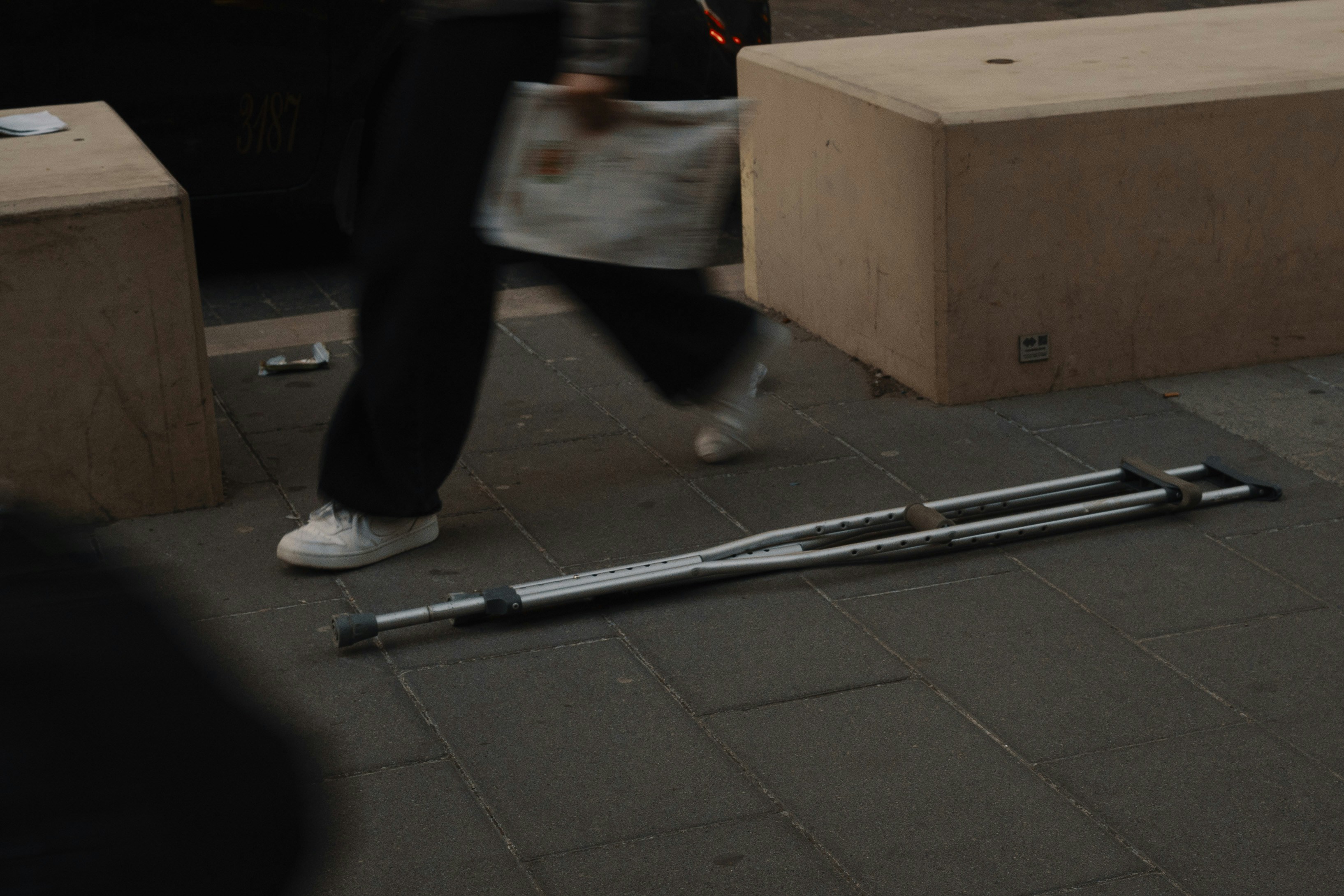 Crutches lying on a sidewalk with person walking