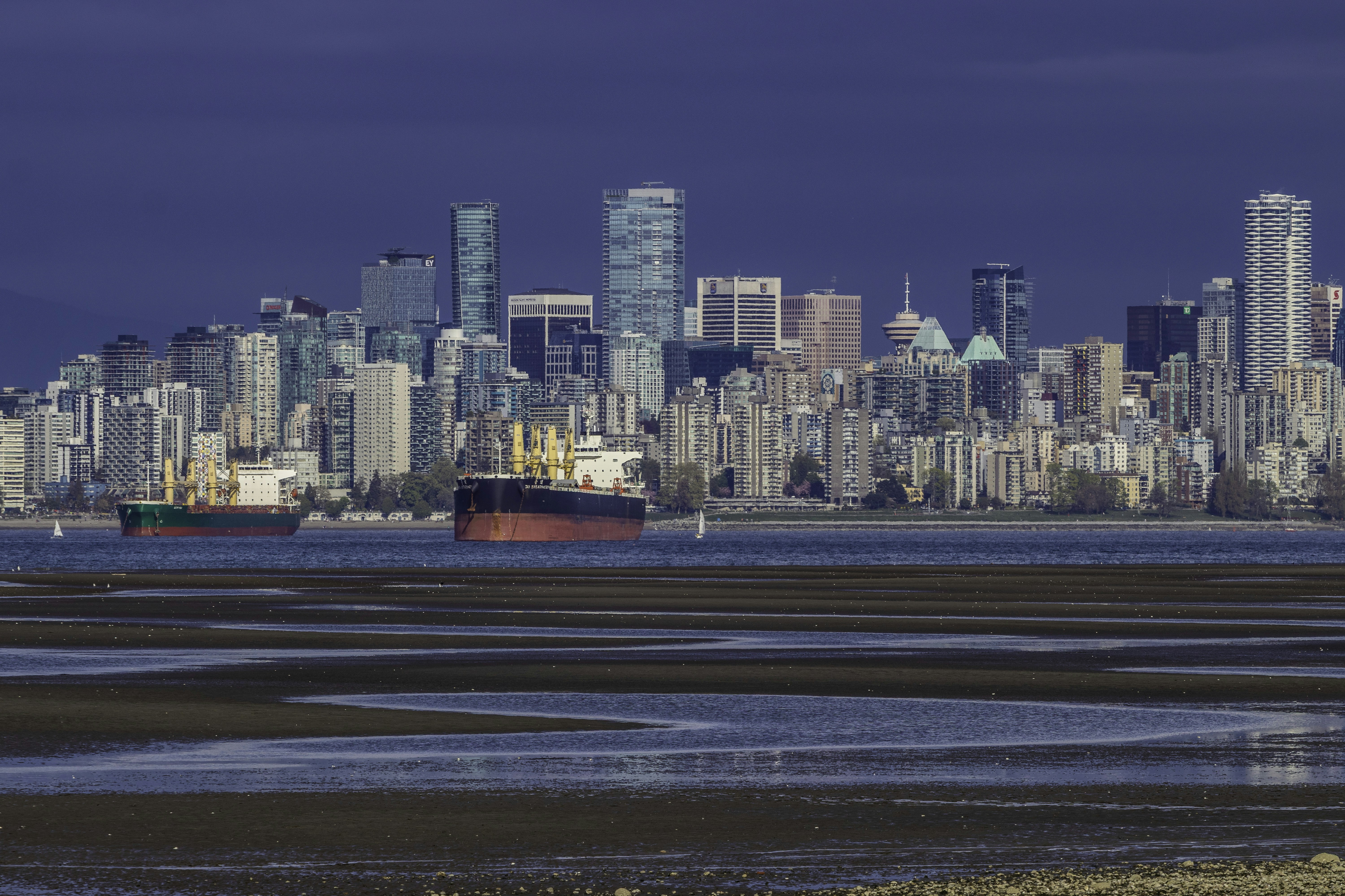 Ships sail past a modern cityscape across the water.