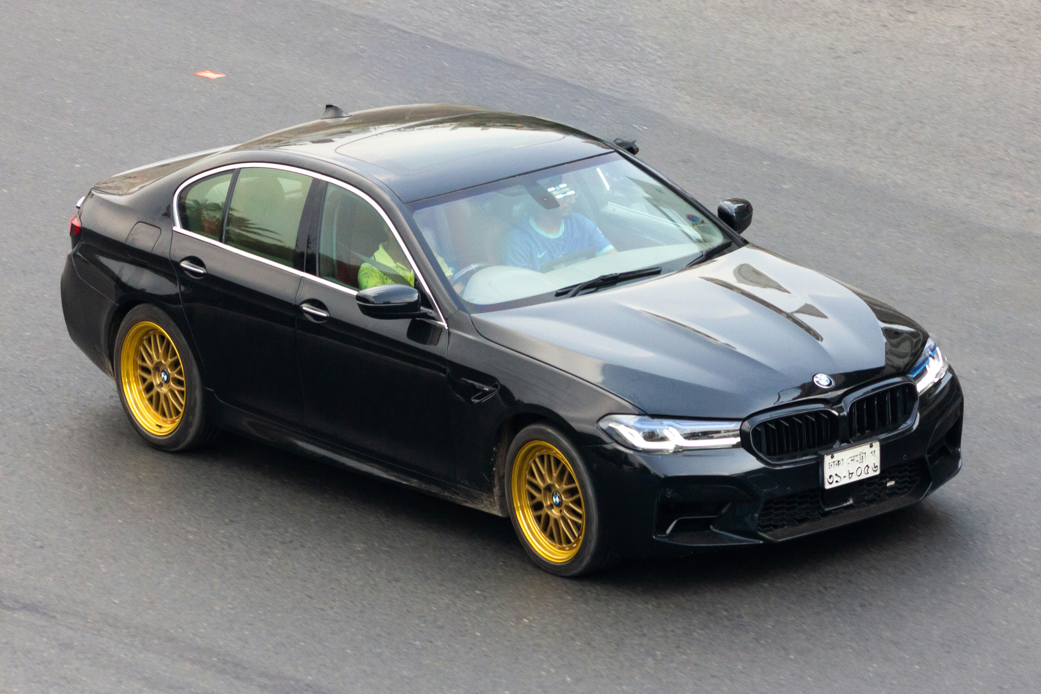 A black BMW sedan with gold rims on a road