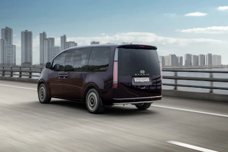 A dark purple minivan drives on a bridge.