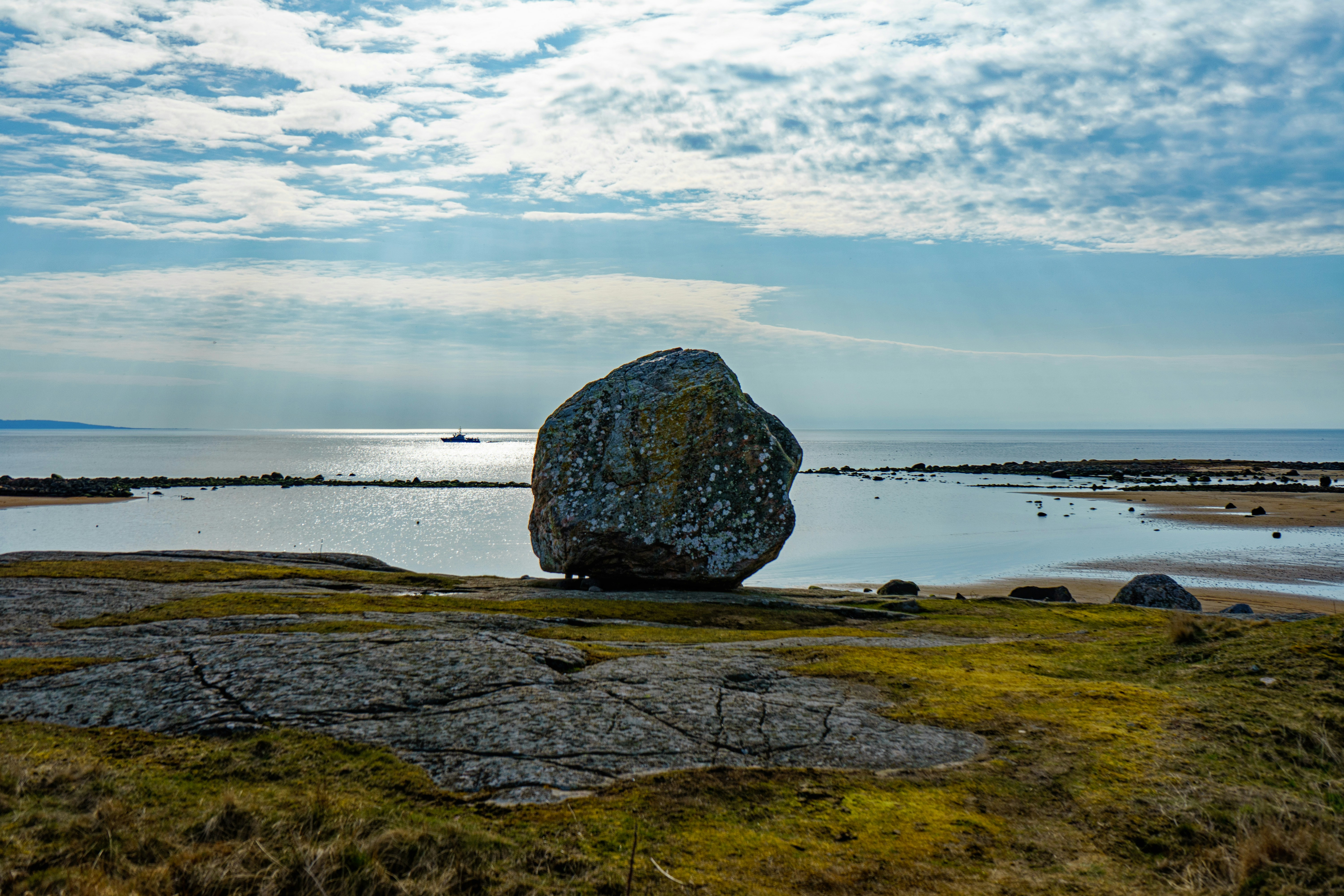 Grande pedra em uma praia gramada perto do oceano.