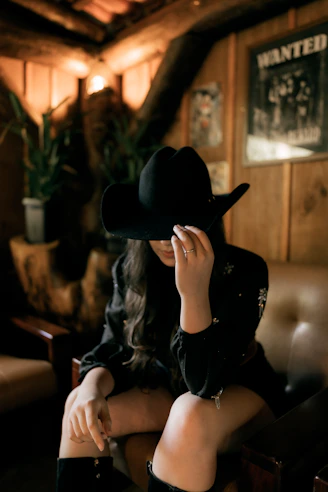 Woman in black cowboy hat sits in dimly lit room.