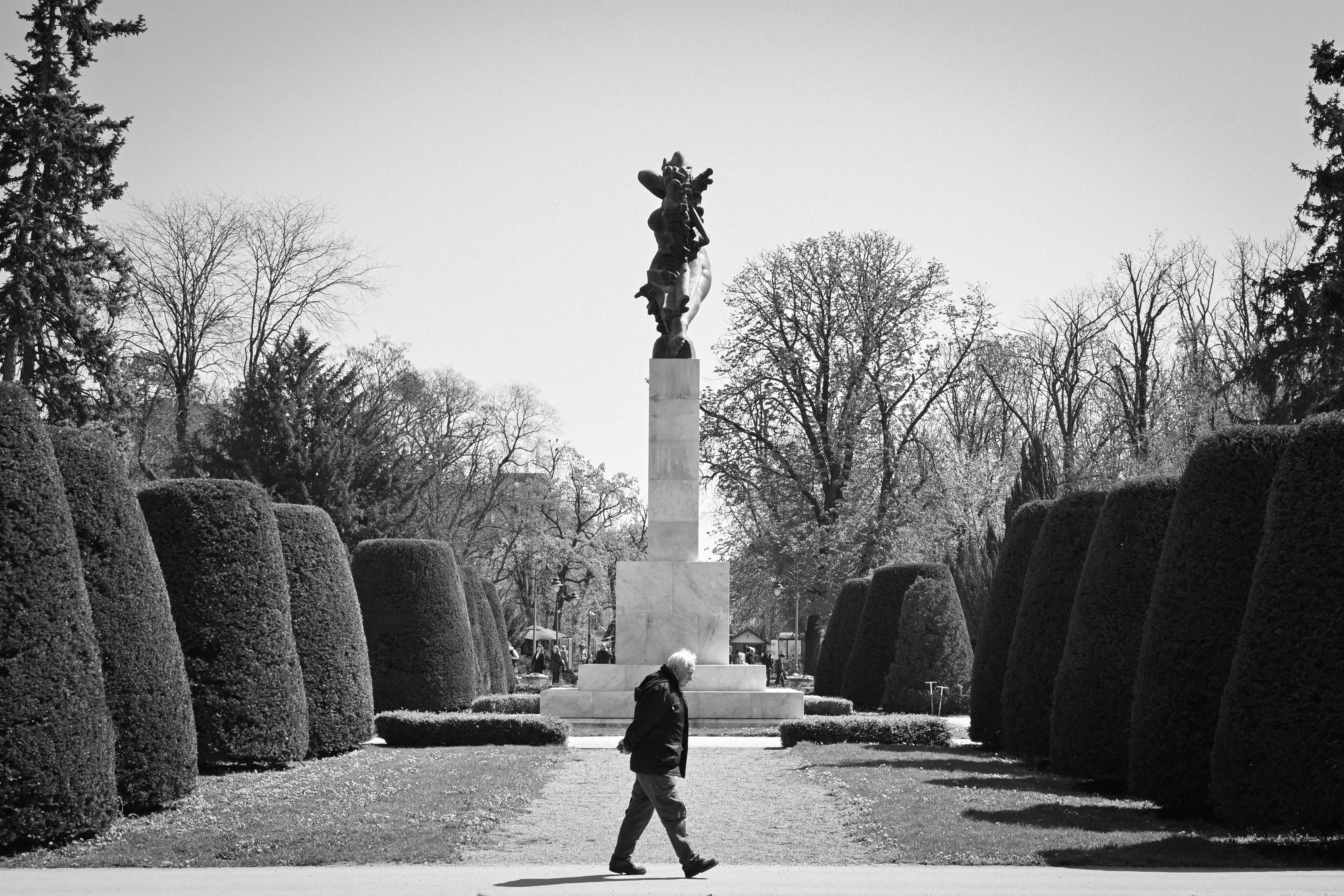 A lone figure walks down a path towards a monument.