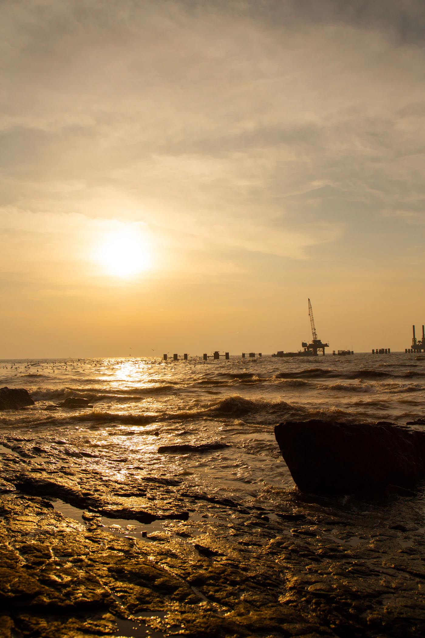 Offshore oil drilling platform silhouetted against an orange and navy sunset sky, representing the maritime industry the Jones Act governs