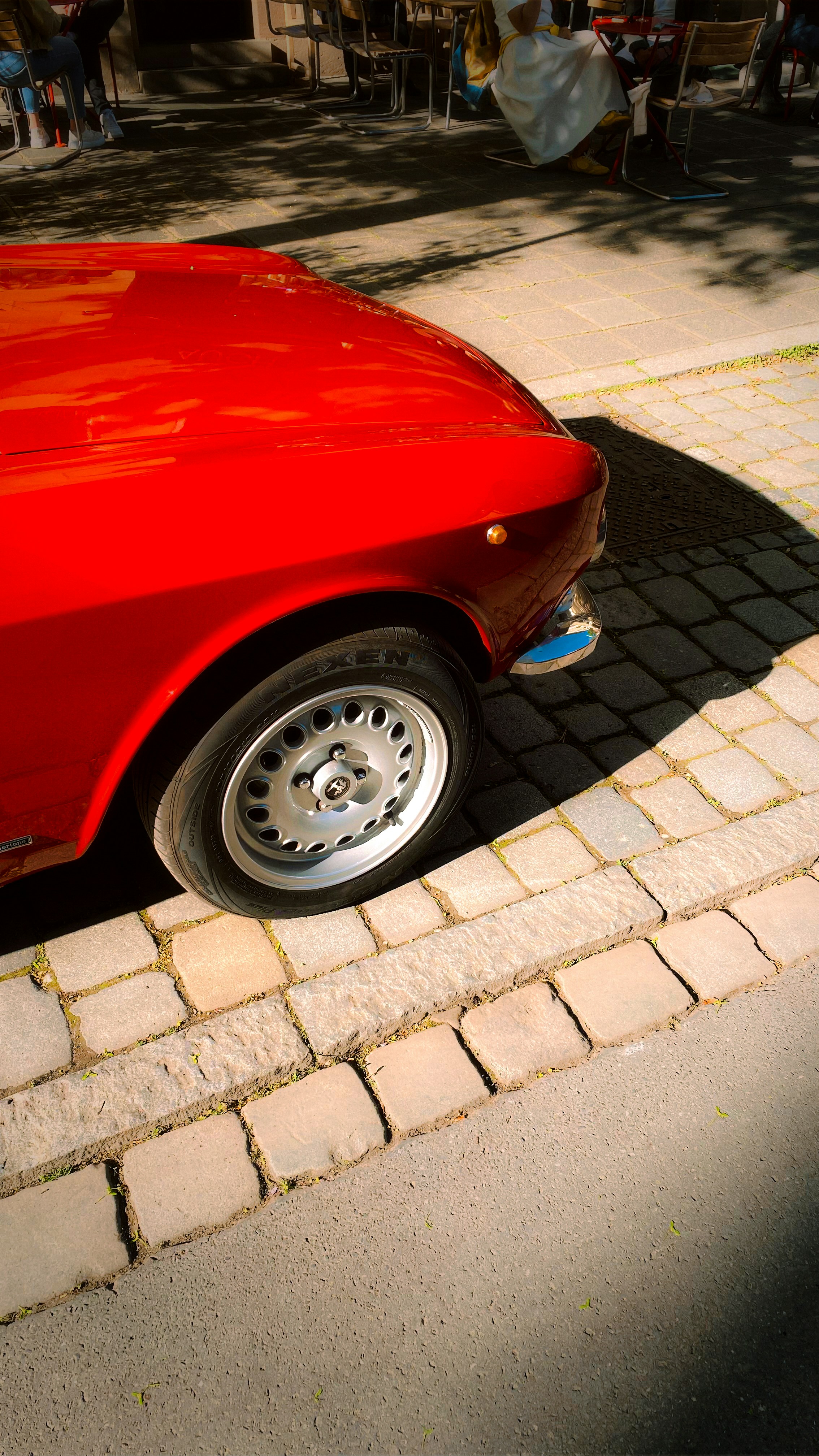 Un'auto d'epoca rossa vivace parcheggiata su una strada di ciottoli.